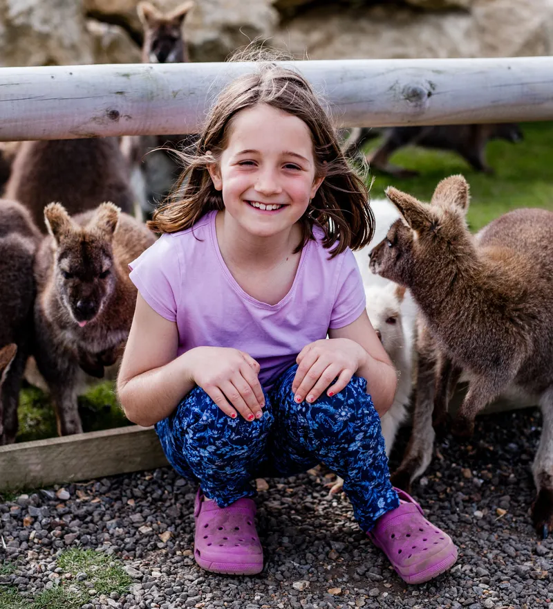 Smiling girl sitting beside wallabies at Tapnell Farm Park