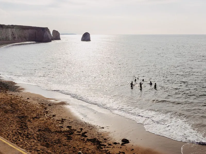 People swimming in the sea beside a sandy beach and chalk cliffs with offshore rock stacks