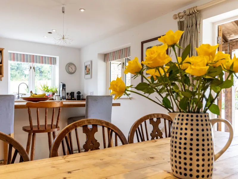 Dining table with yellow roses in a jug in a bright cottage kitchen