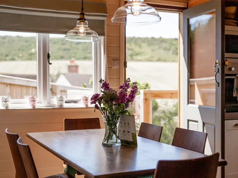Cosy dining table with fresh purple flowers in a bright kitchen, with open door and countryside views beyond