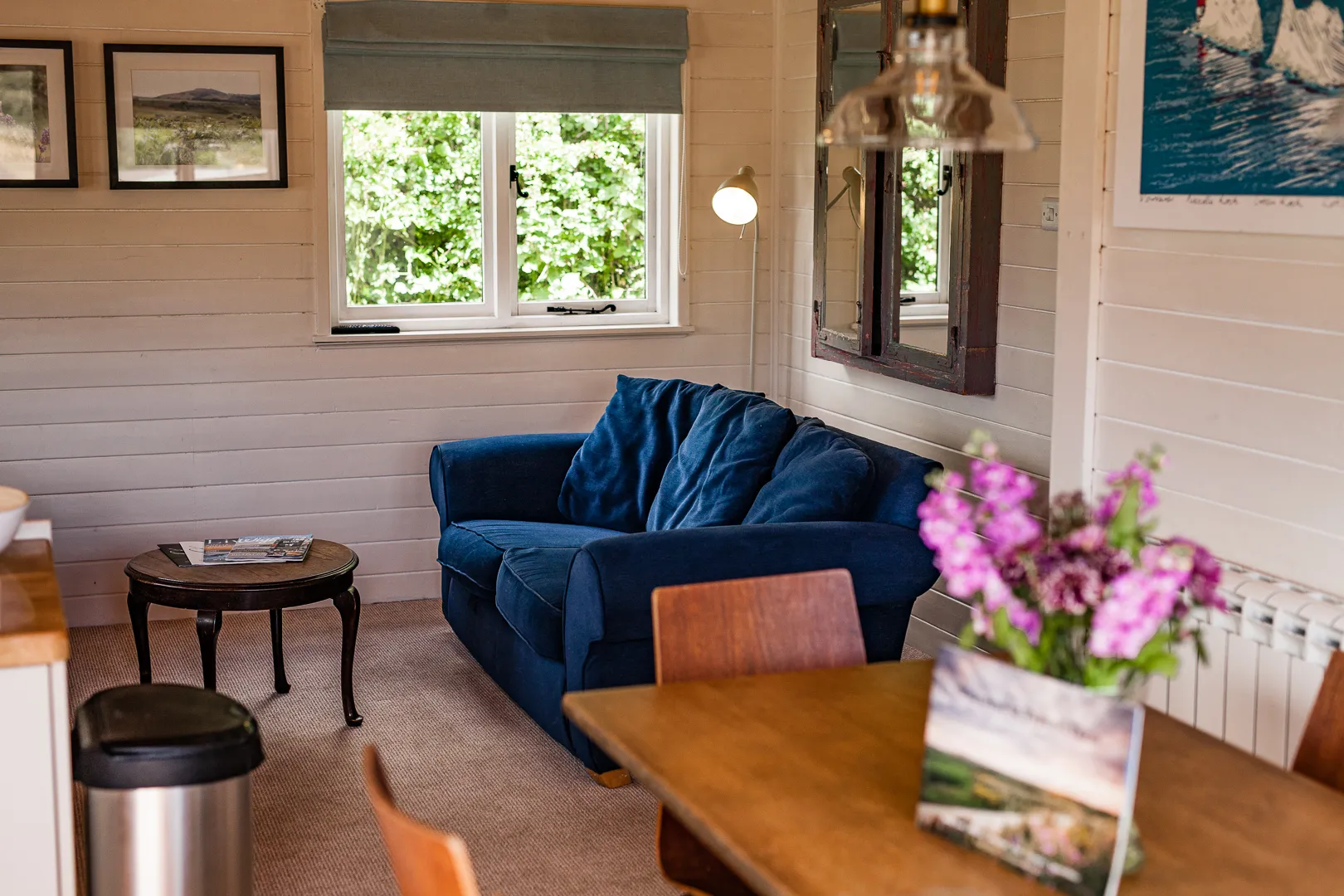 Cosy cabin sitting area with a deep blue sofa, small coffee table, and window looking onto greenery