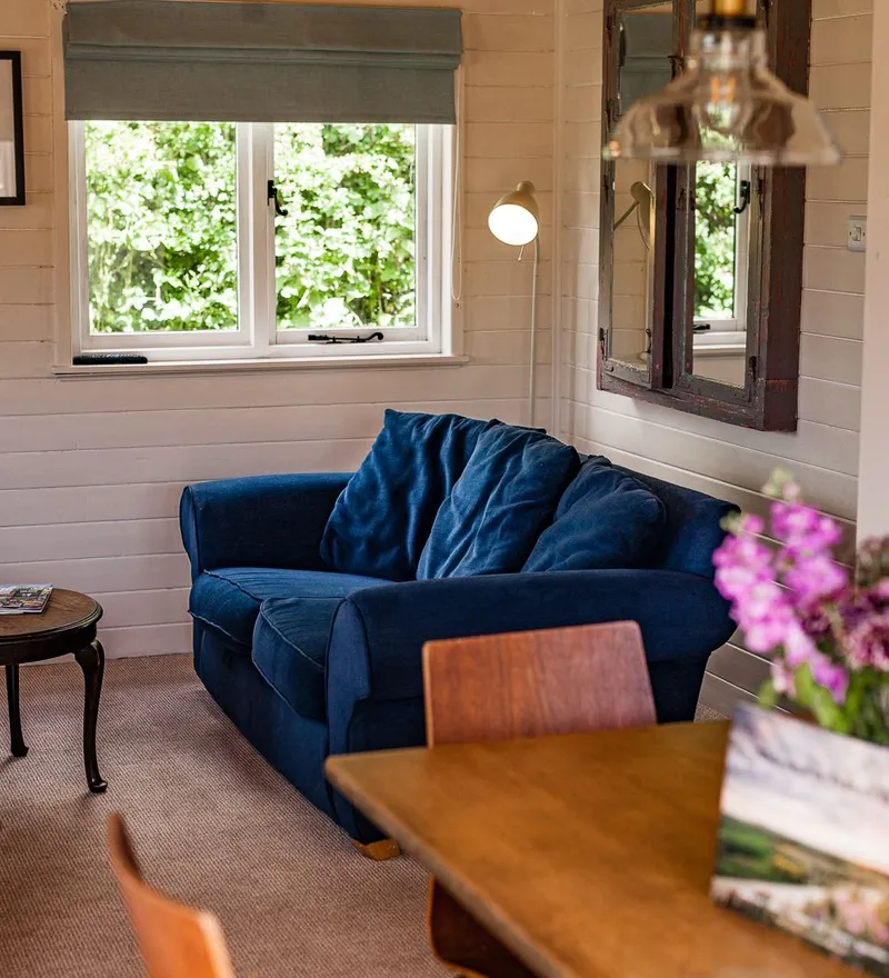Cosy cabin sitting area with a deep blue sofa, small coffee table, and window looking onto greenery