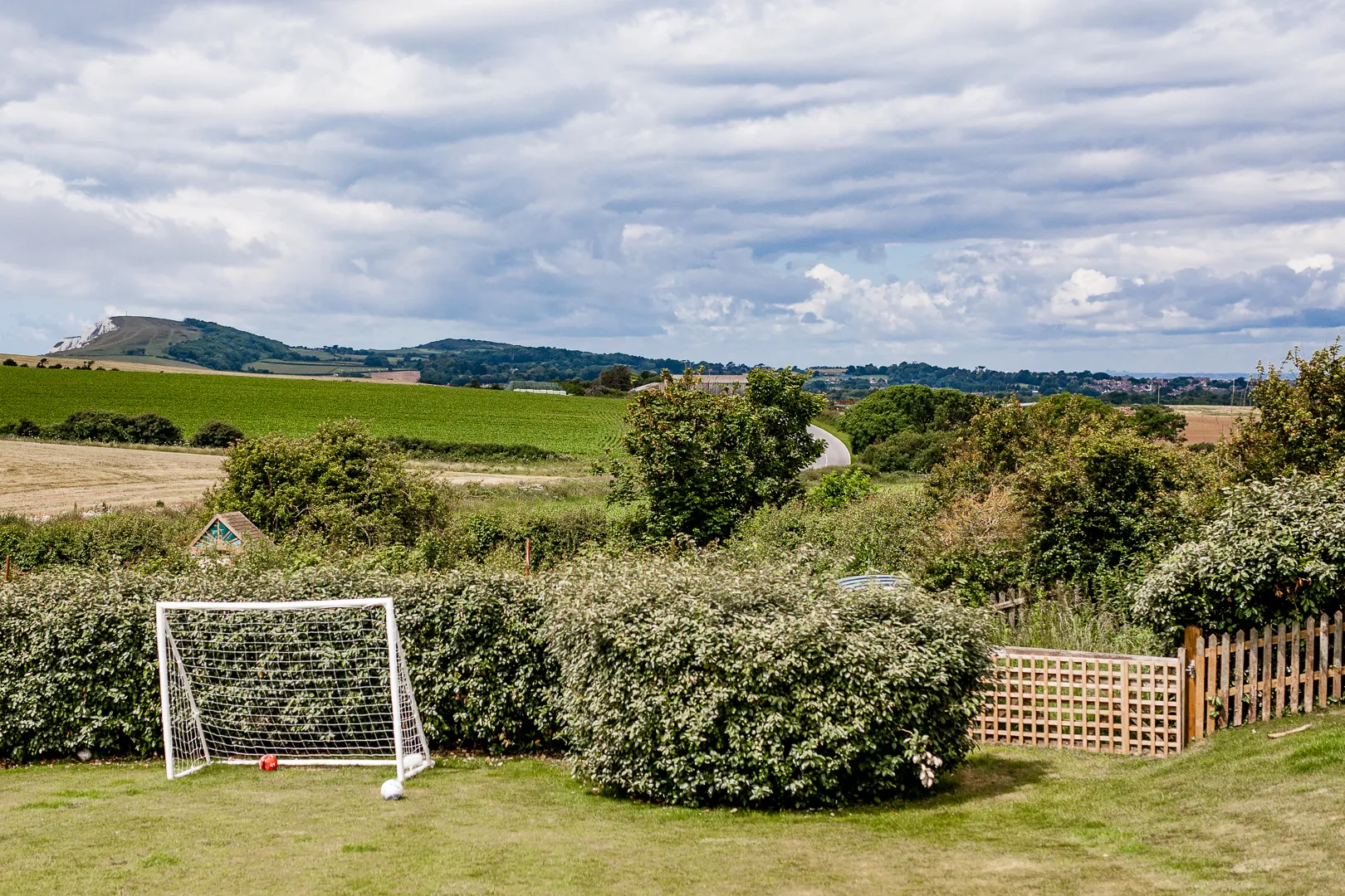 Garden with a football goal and balls overlooking green countryside fields under a cloudy sky