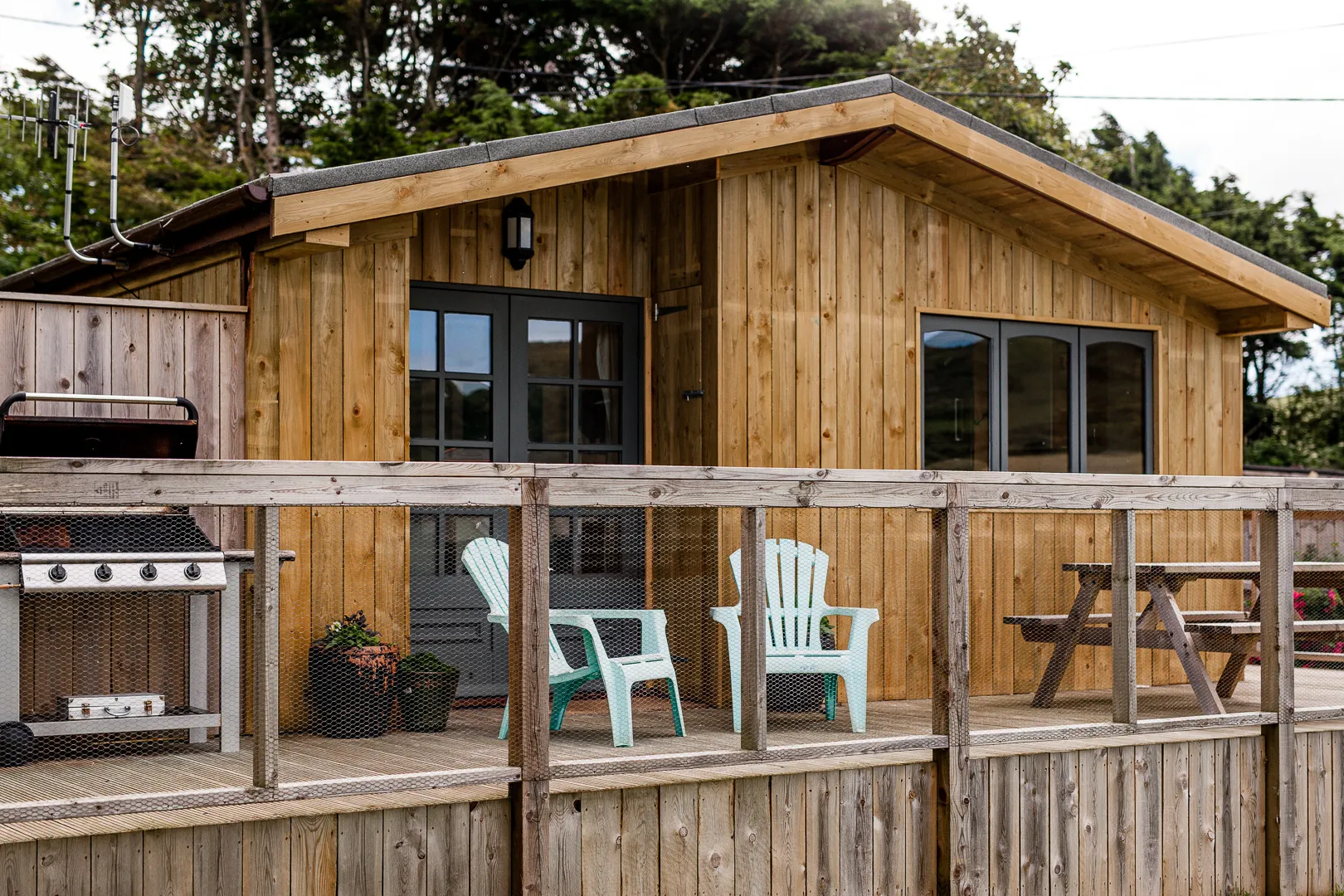 Wooden cabin with a deck, barbecue, outdoor chairs and picnic table