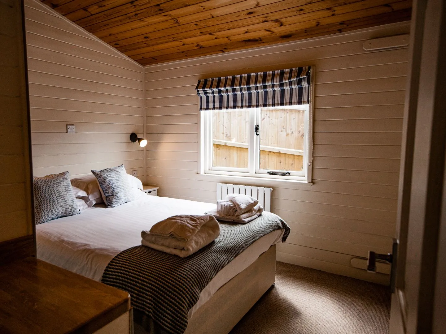 Cosy double bedroom with wooden ceiling, striped blind and neatly folded towels on the bed
