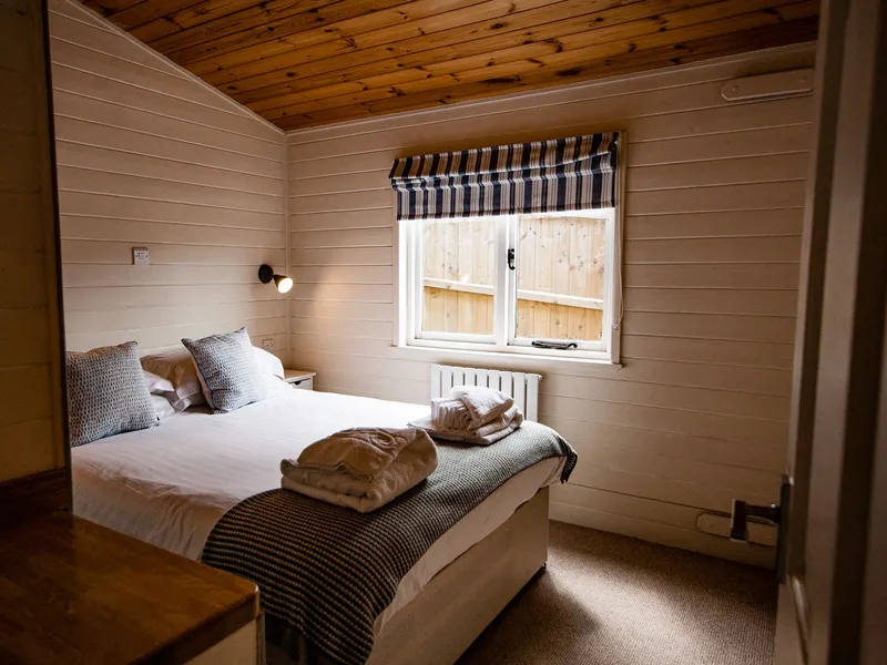 Cosy double bedroom with wooden ceiling, striped blind and neatly folded towels on the bed