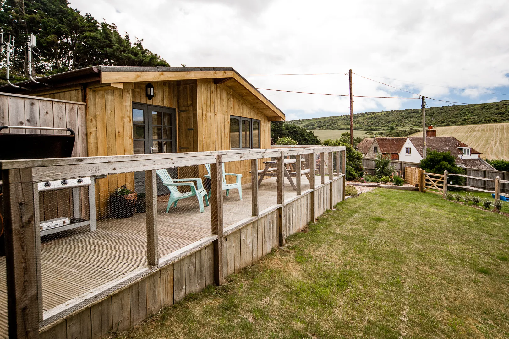 Wooden lodge with deck, outdoor chairs and grassy garden overlooking countryside