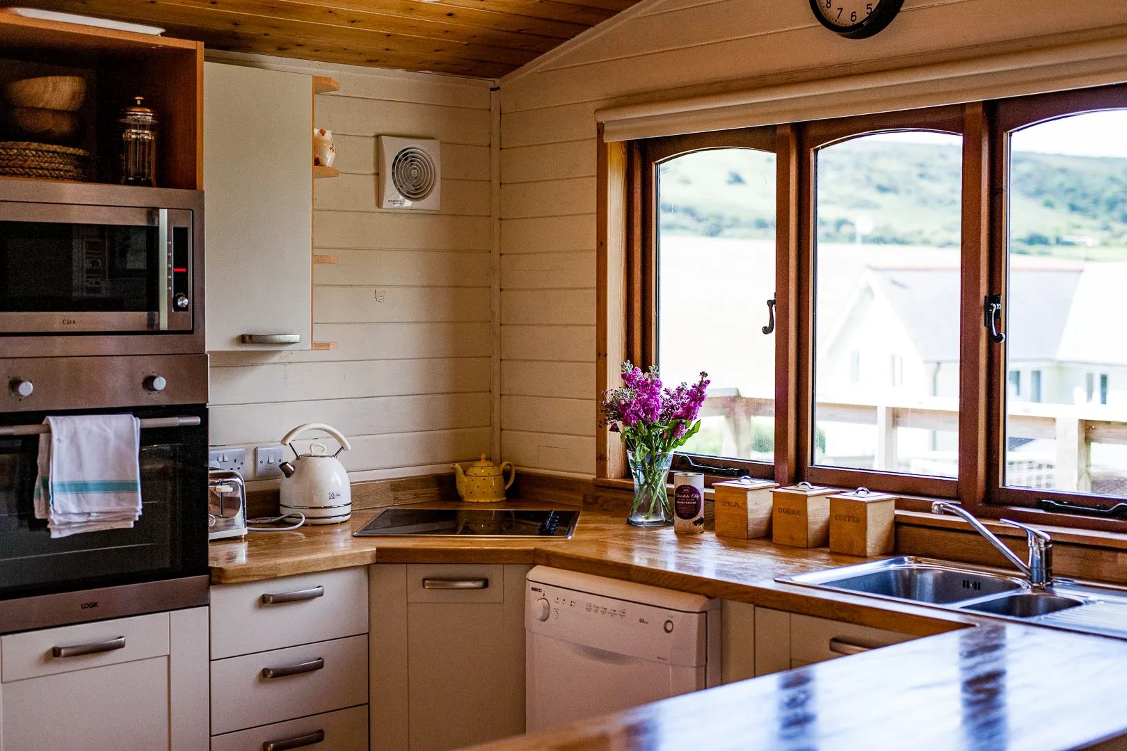 Cosy wooden kitchen with sink, appliances and large window overlooking countryside and water