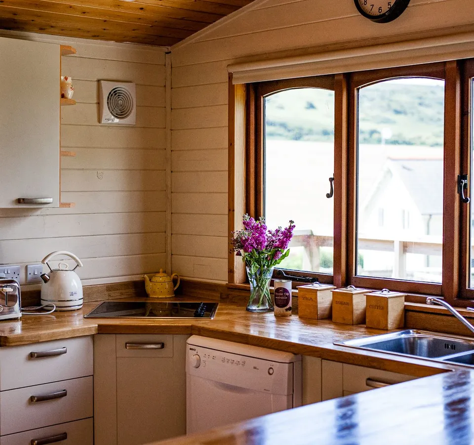 Cosy wooden kitchen with sink, appliances and large window overlooking countryside and water