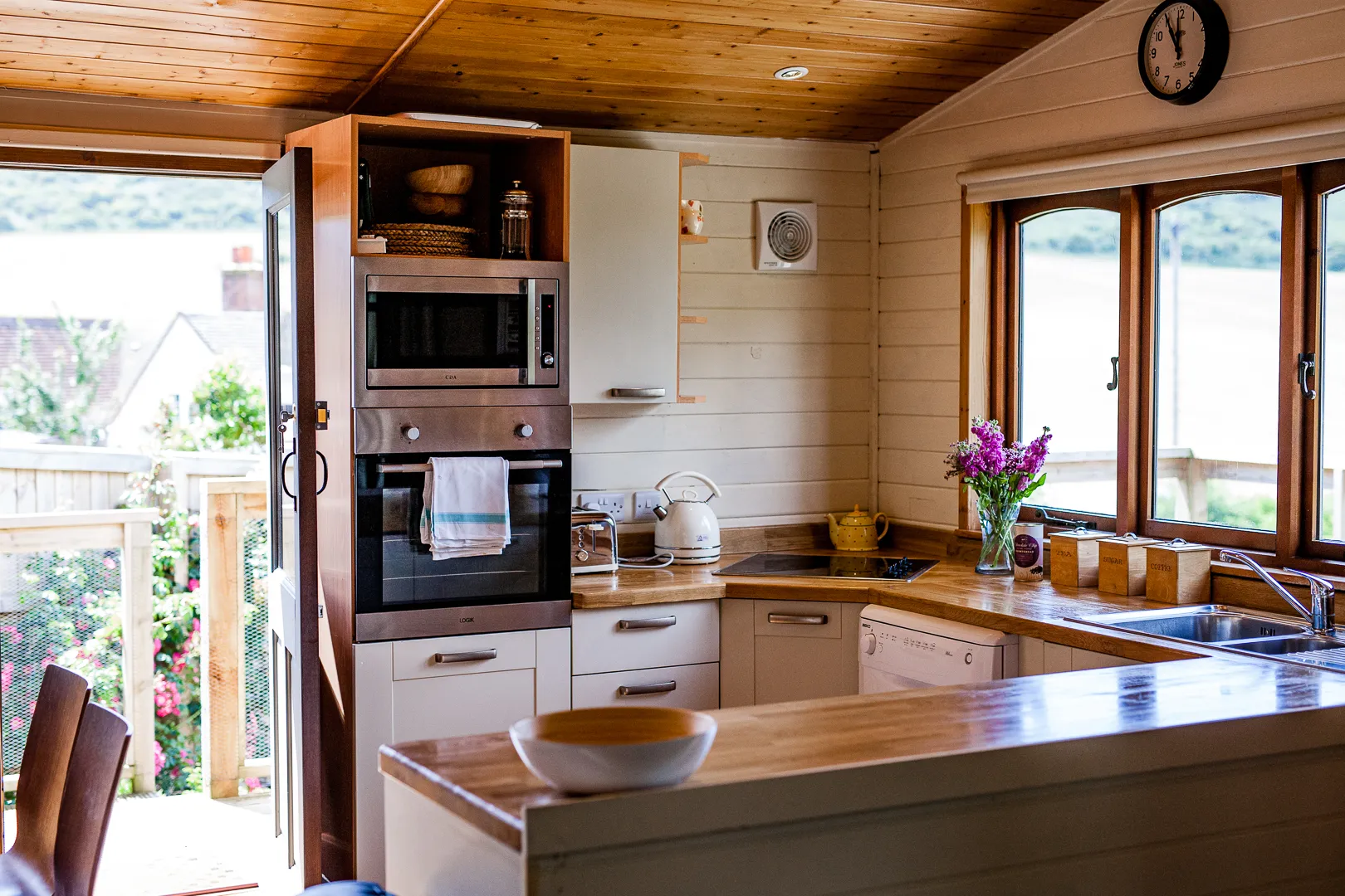 Cosy wooden lodge kitchen with built-in oven, pale cabinets and large window overlooking the water