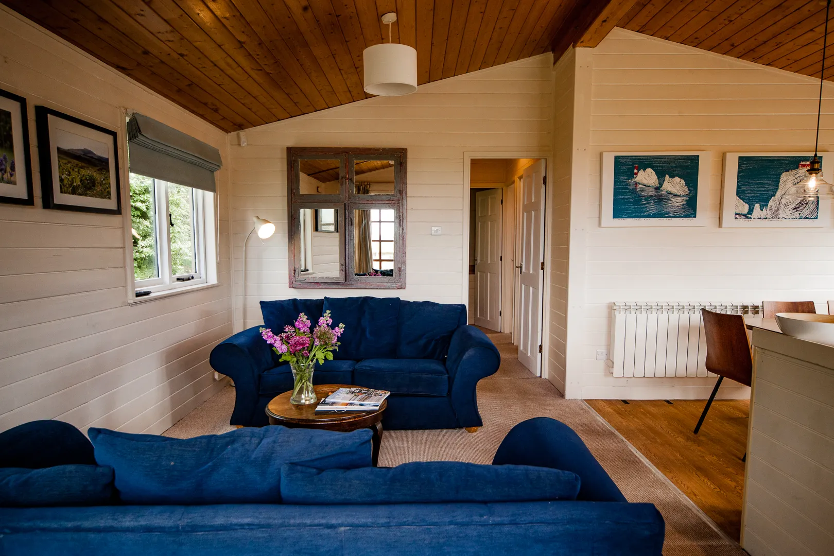 Cosy cabin lounge with blue sofas, wooden ceiling, coffee table with flowers and wall art