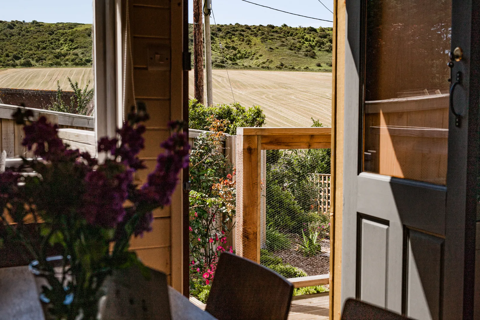 Open door looking out to a wooden deck and garden with rolling green hills and fields beyond