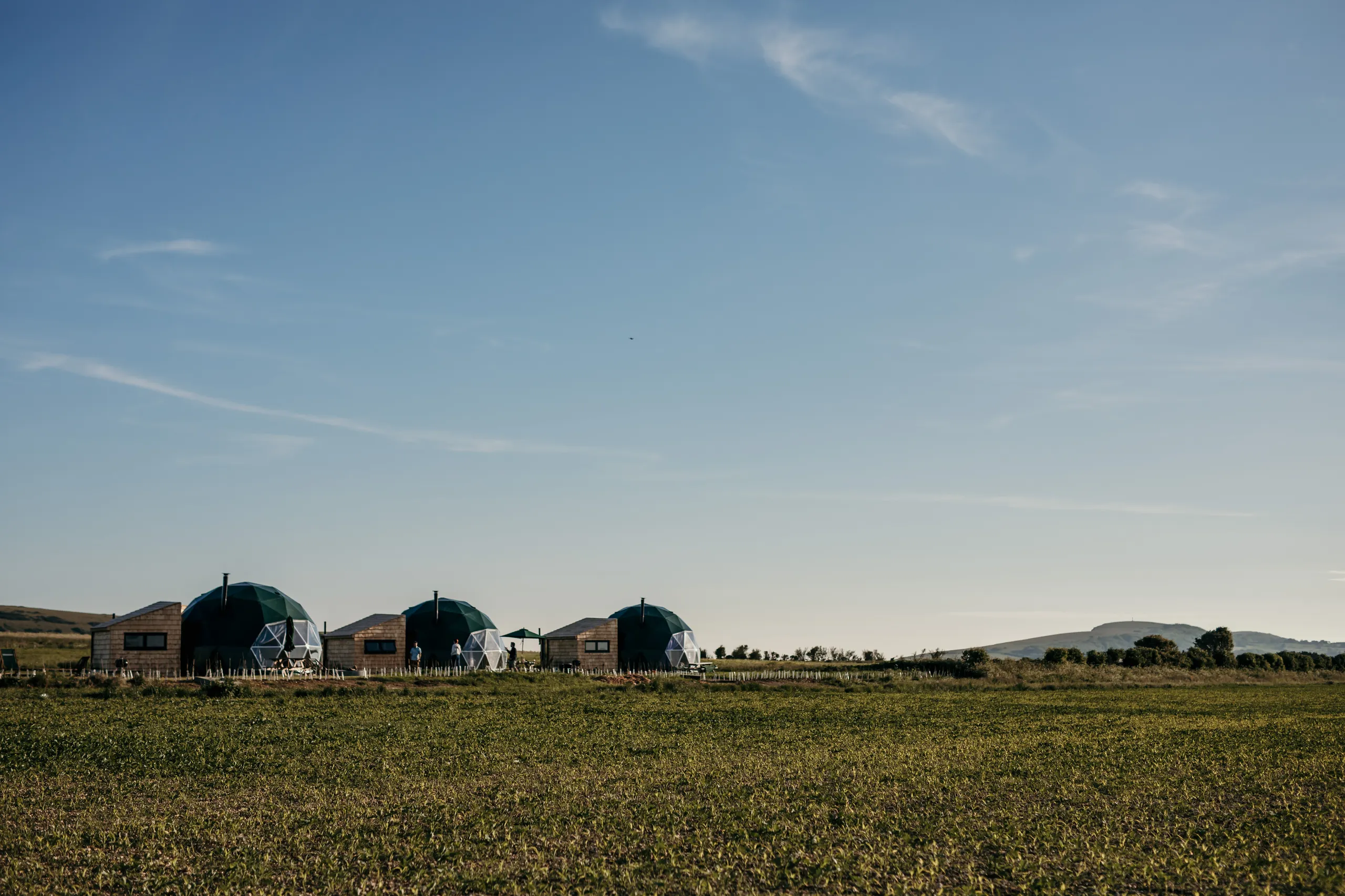 Geodesic dome cabins in a grassy field beneath a wide blue sky
