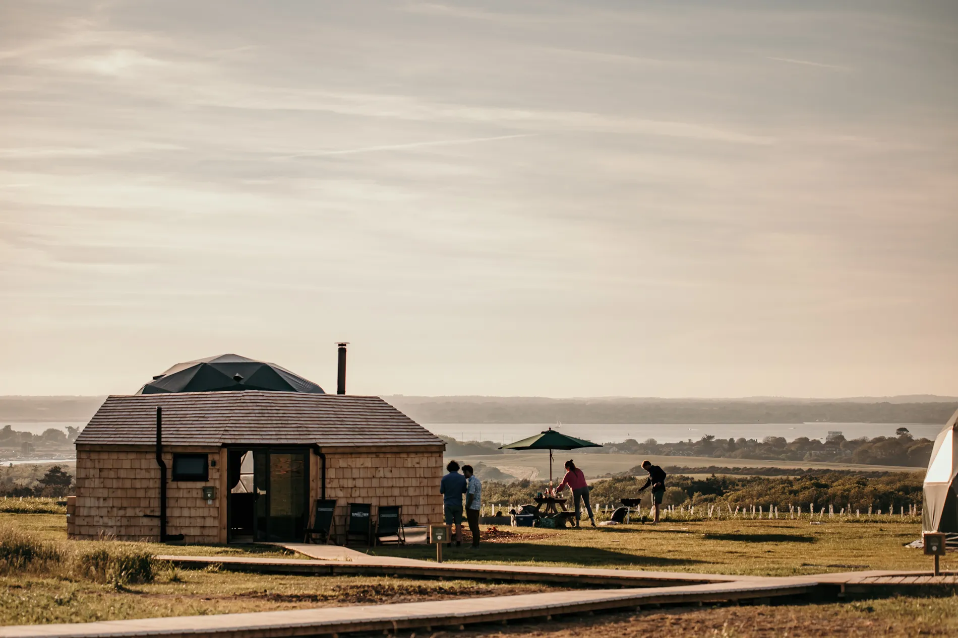 Family outside a glamping dome cabin on a hillside with a sea view at sunset