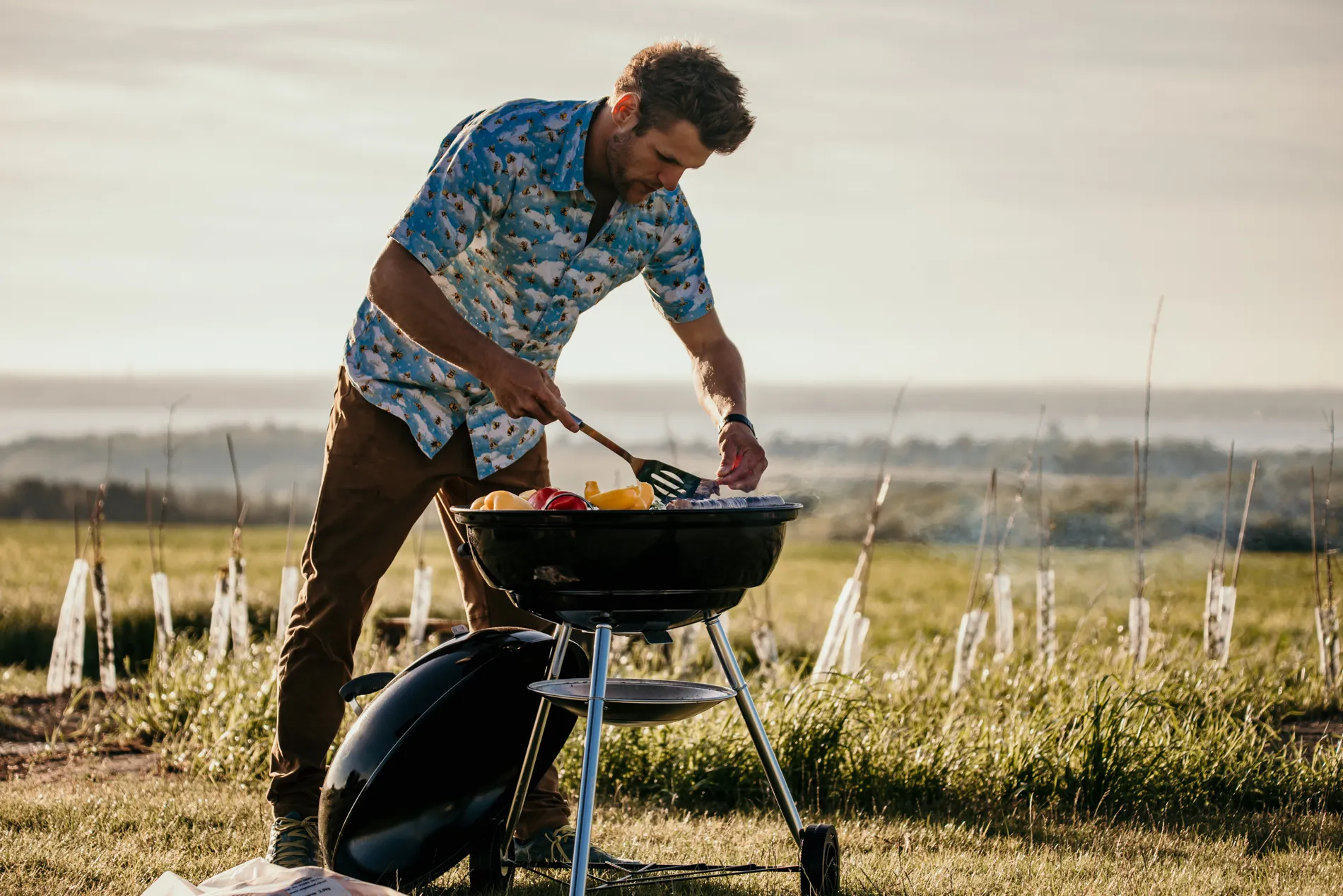 Man grilling food on a barbecue in a grassy field at sunset