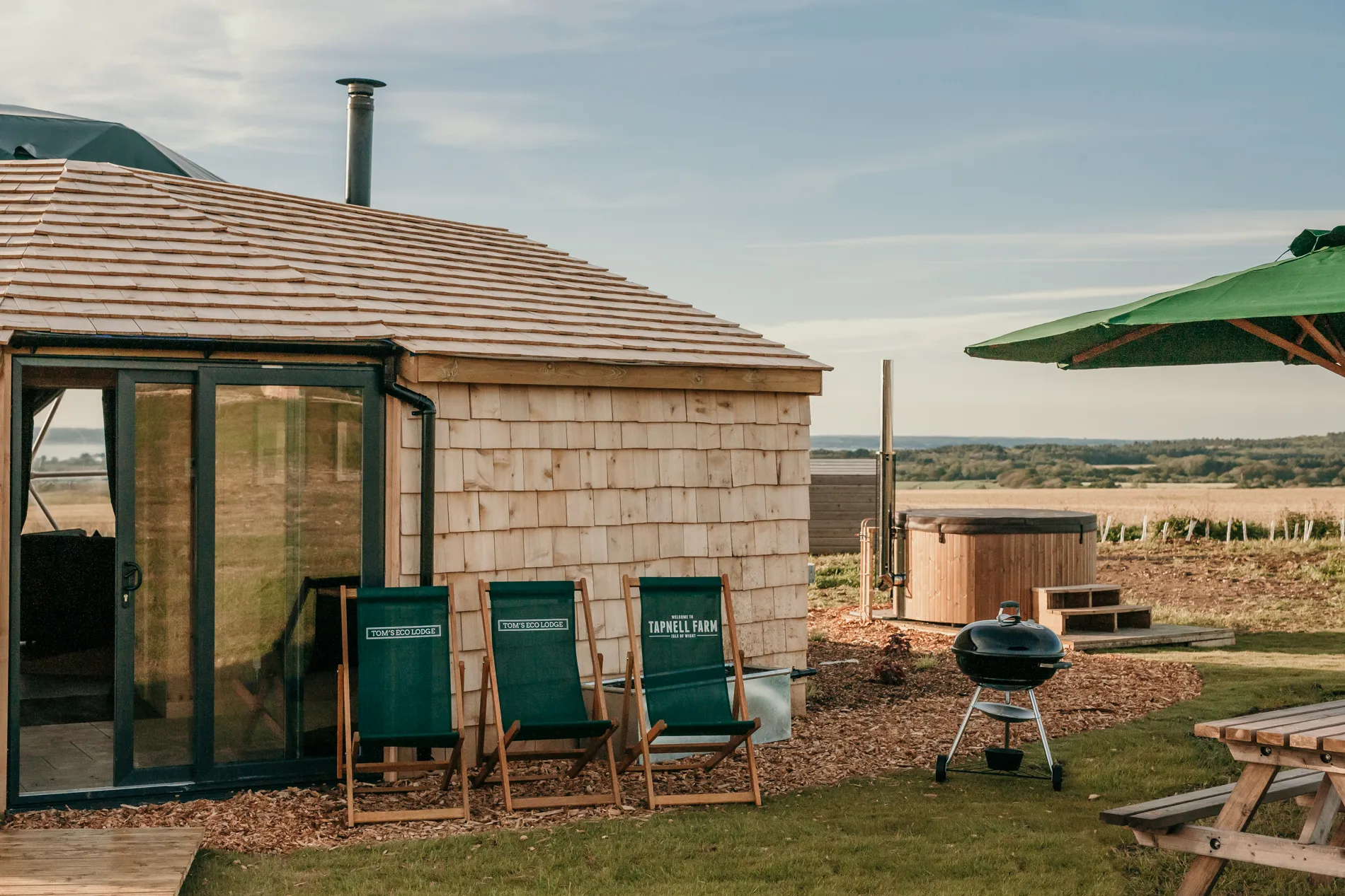 Eco lodge with wooden shingle cladding, deckchairs and outdoor hot tub overlooking countryside