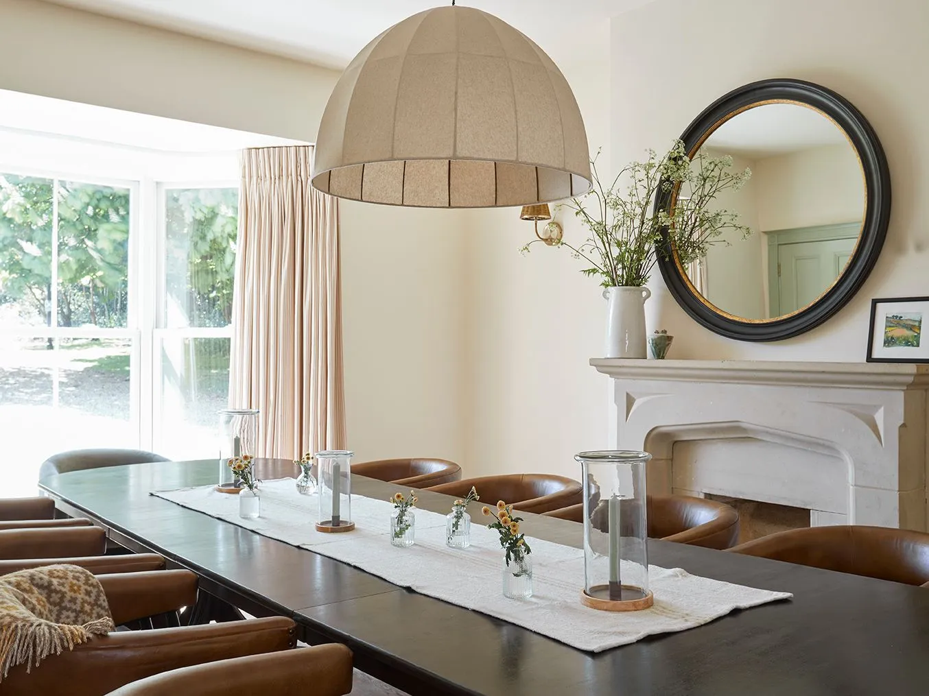 Dining room with long table, leather chairs, large pendant light and fireplace with round mirror