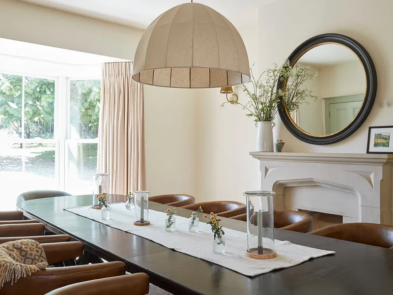 Dining room with long table, leather chairs, large pendant light and fireplace with round mirror