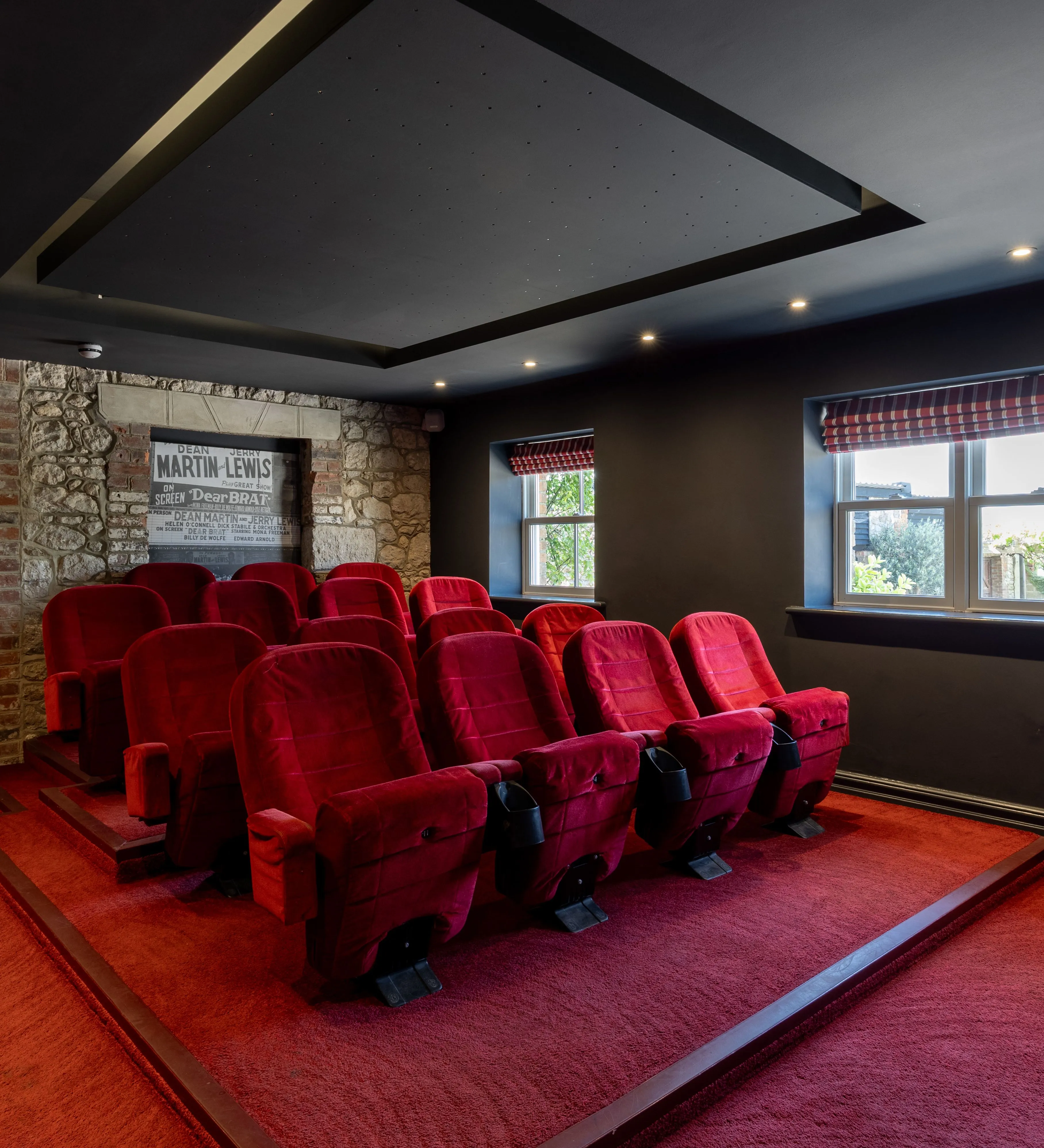 Home cinema room with tiered red velvet seats, dark walls and a stone feature wall