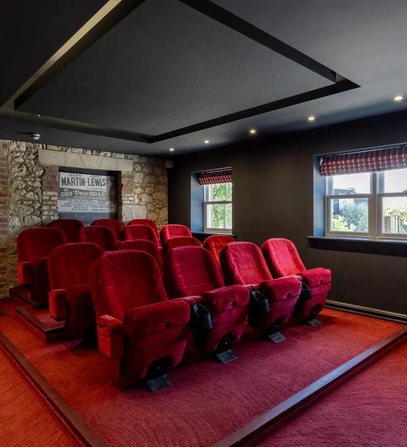 Home cinema room with tiered red velvet seats, dark walls and a stone feature wall
