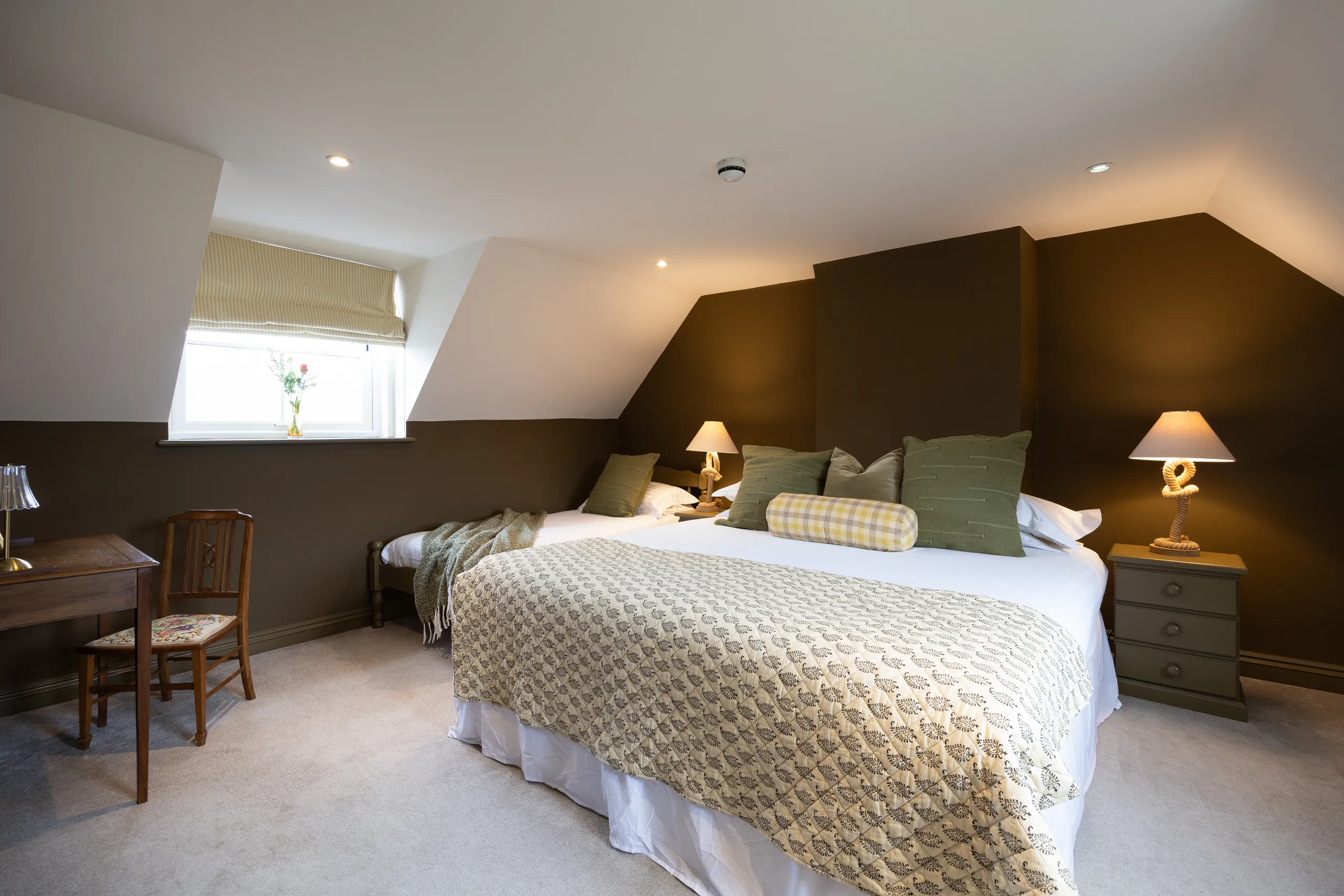 Cosy attic bedroom with double bed, green cushions and bedside lamps, plus a desk by the window