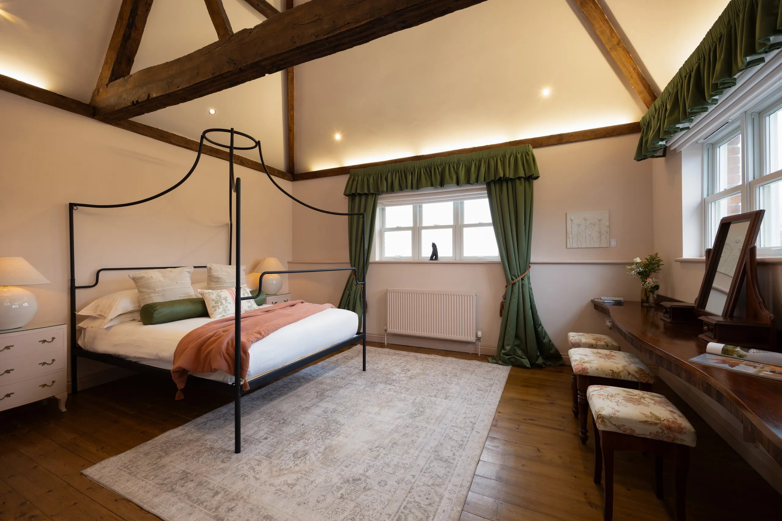 Rustic farmhouse bedroom with exposed timber beams, black metal four-poster bed, and green curtains