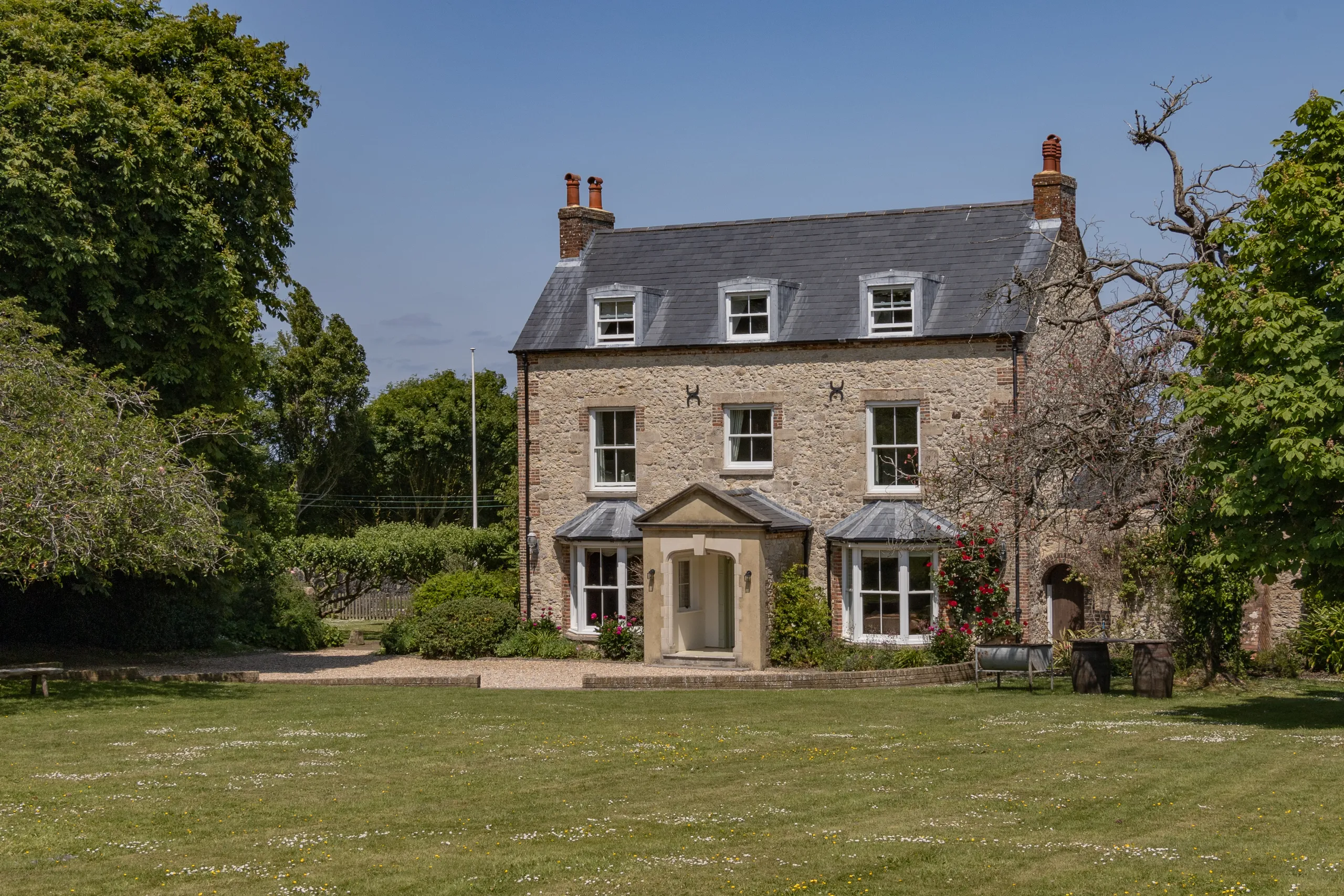 Stone farmhouse with slate roof and dormer windows, set in a green garden under a clear blue sky