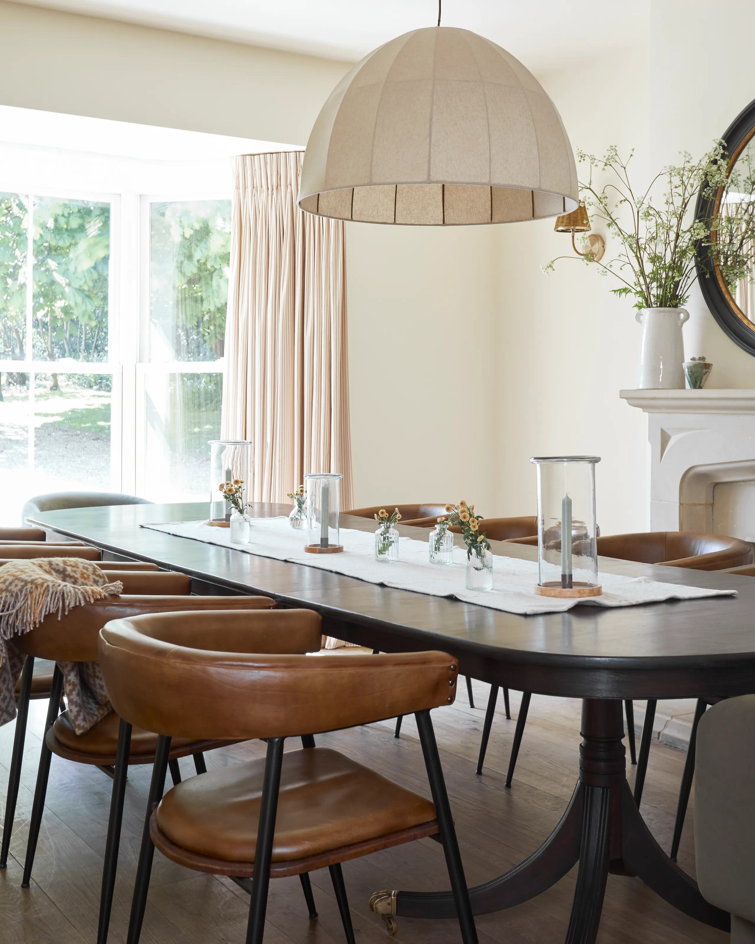 Bright farmhouse dining room with long dark table, tan leather chairs and large dome pendant light