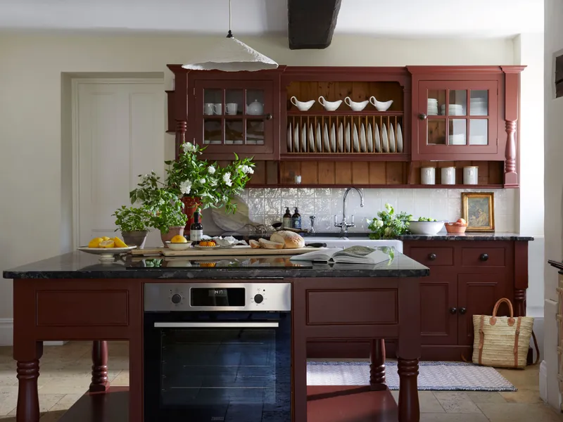Traditional farmhouse kitchen with red wooden cabinets, a central island and open plate rack, styled with flowers, bread and lemons