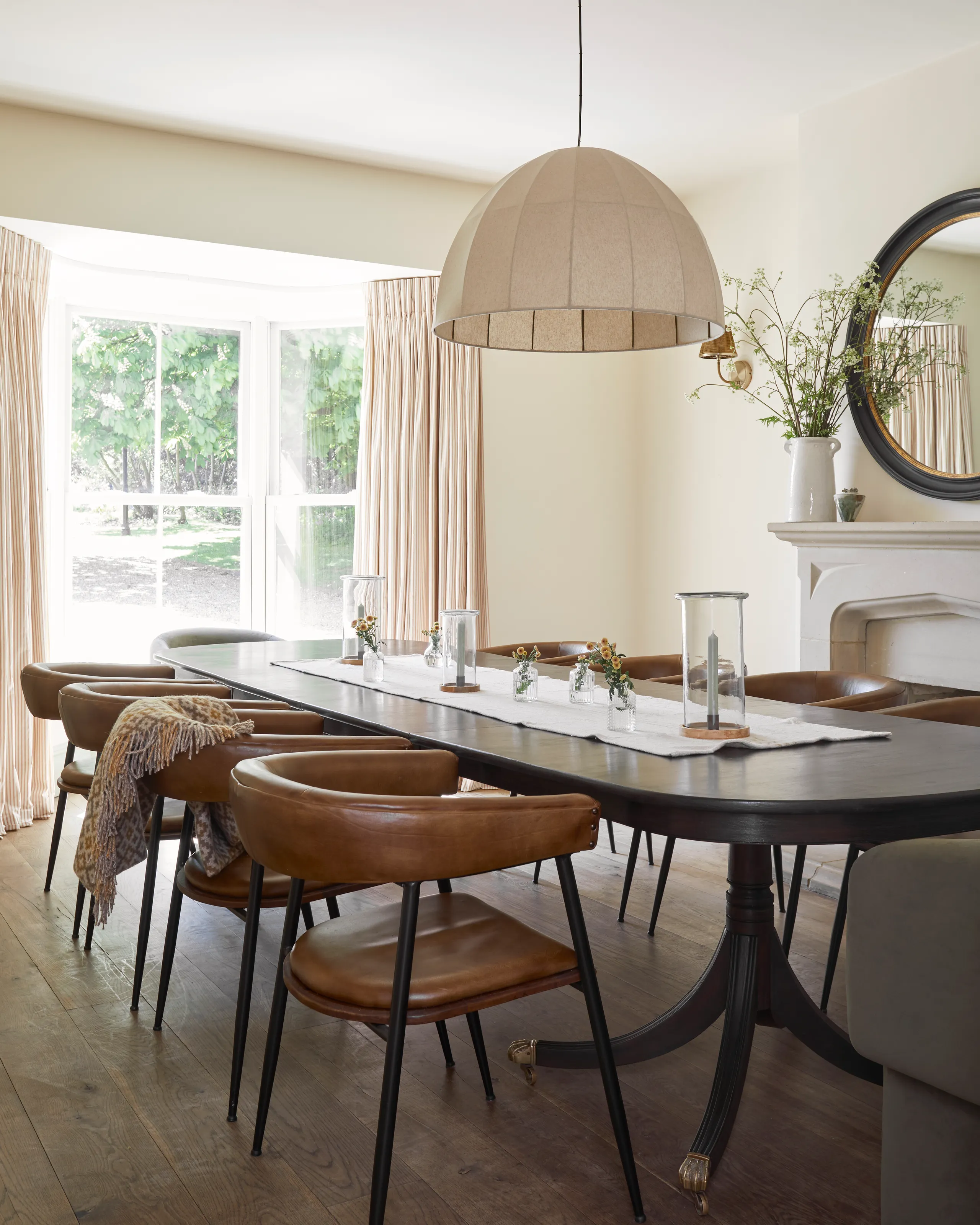 Light-filled farmhouse dining room with dark oval table, tan leather chairs and large pendant shade