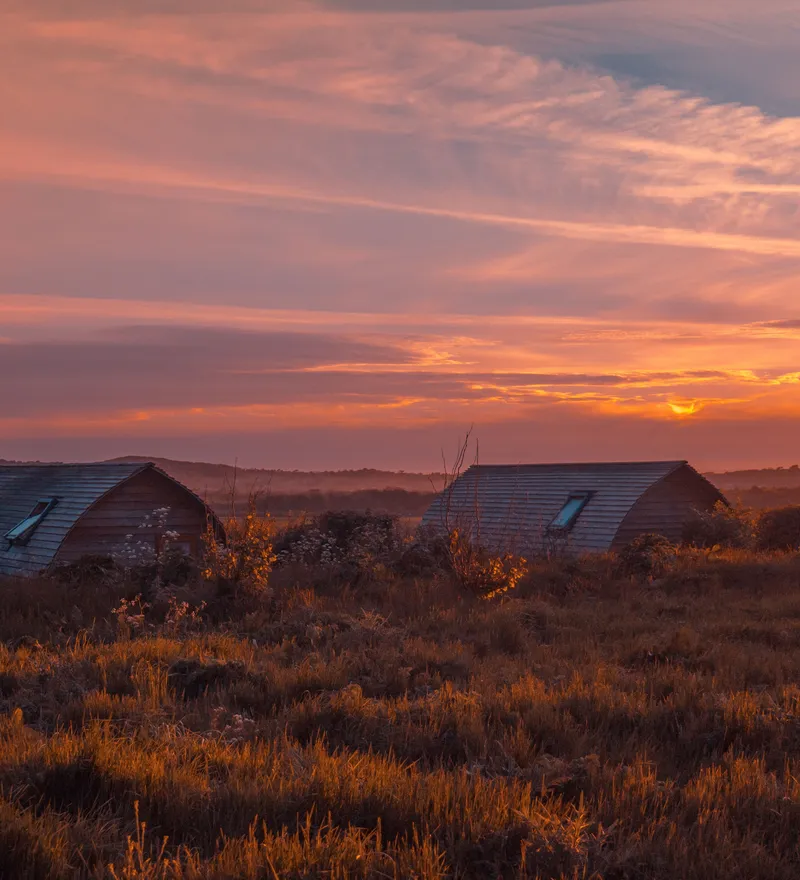 Eco pods at Tapnell Farm with a sunset sky in the background