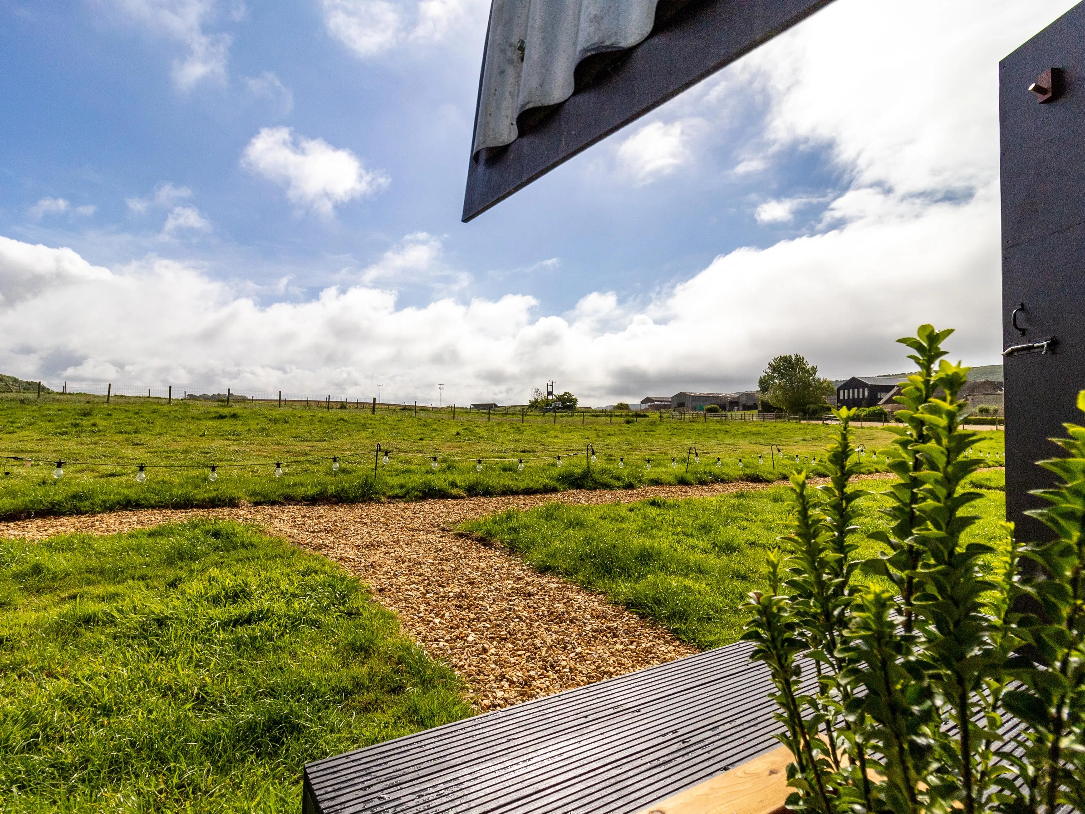 View from a doorway over a grassy field with a winding gravel path and string lights under a blue sky