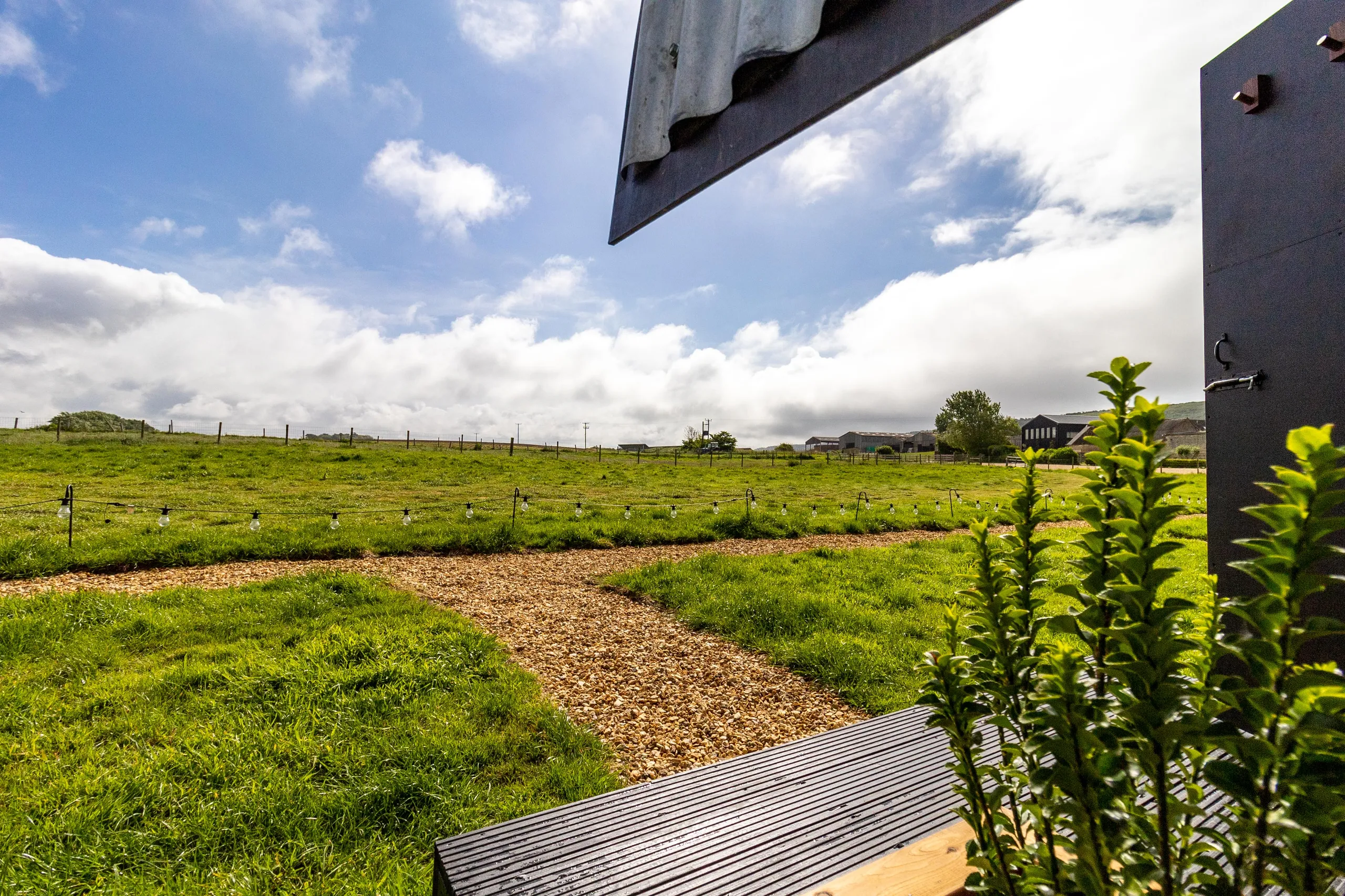 View from a doorway over a grassy field with a winding gravel path and string lights under a blue sky