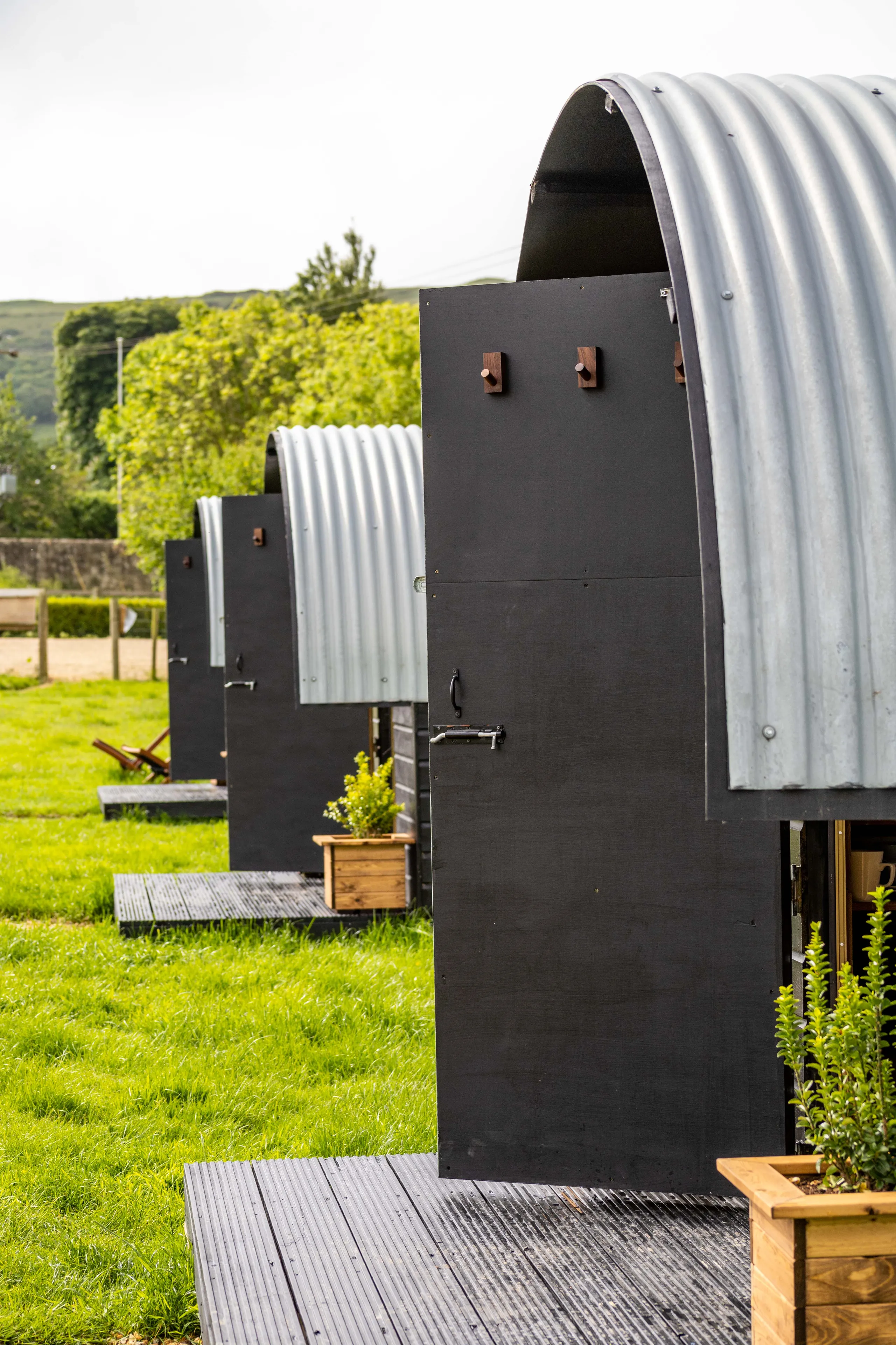 Row of corrugated metal pod cabins with black doors on a grassy field