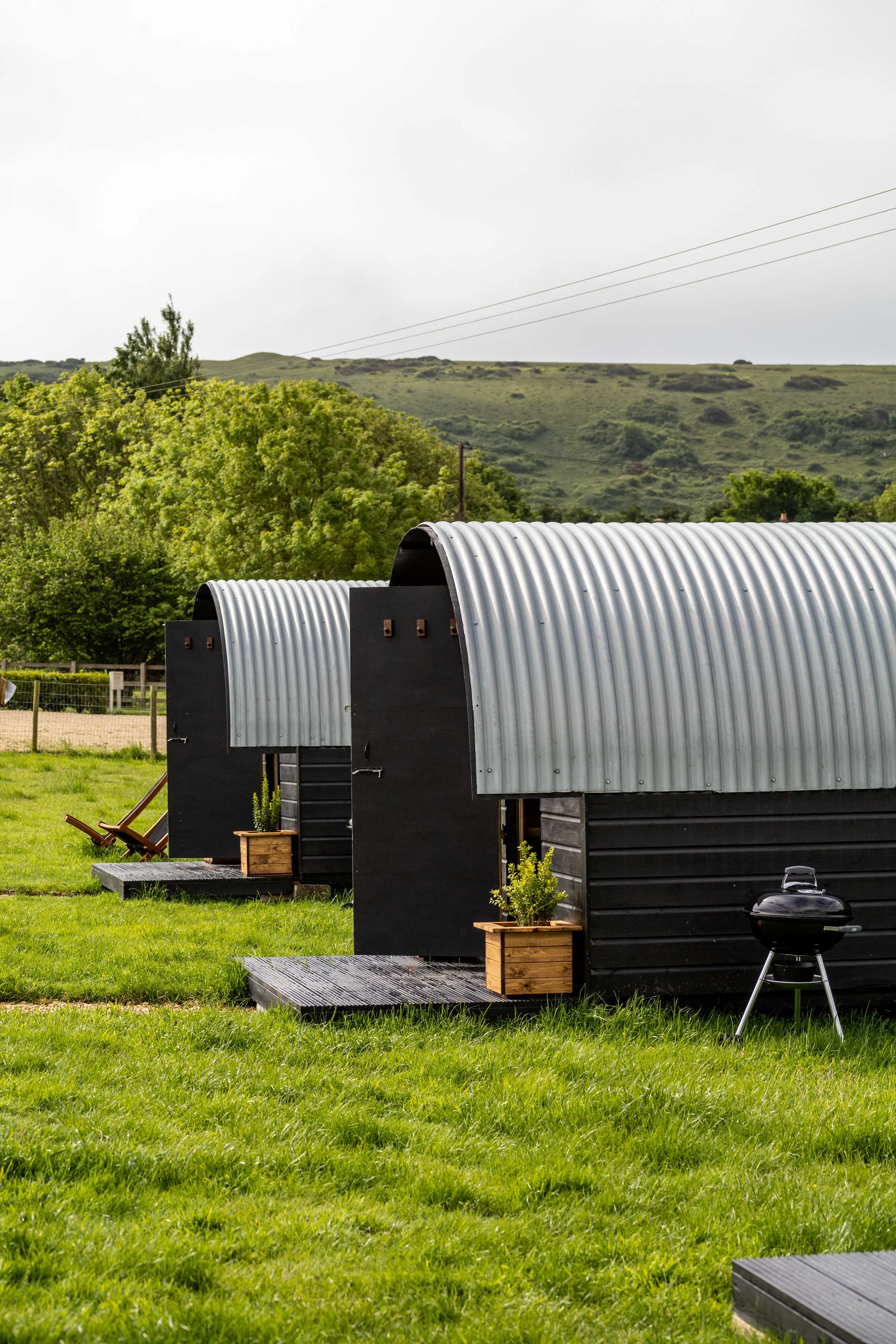 Two corrugated metal huts on a grassy field with hills in the background