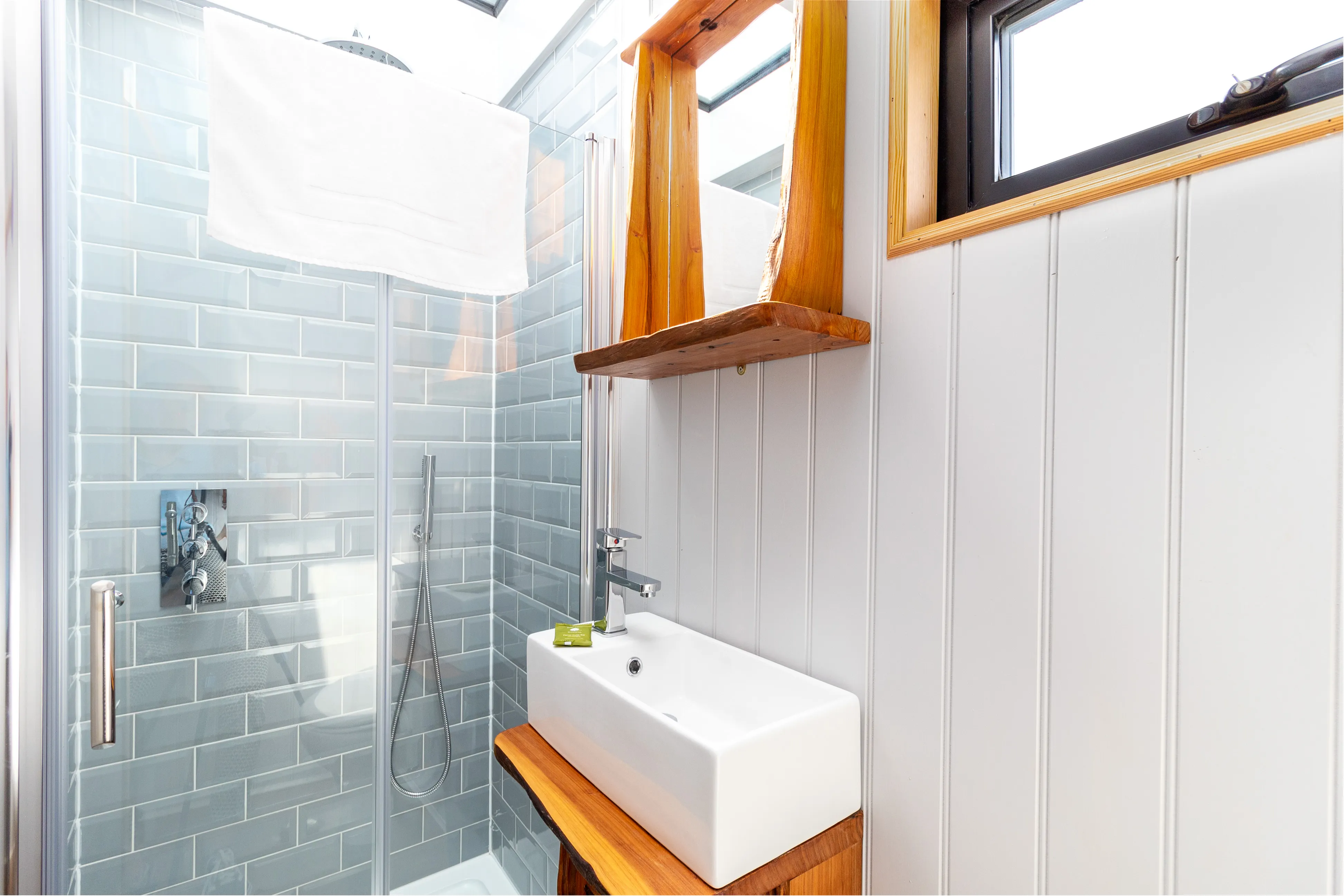 Bright modern bathroom with glass shower, grey subway tiles, and white basin on a wooden vanity