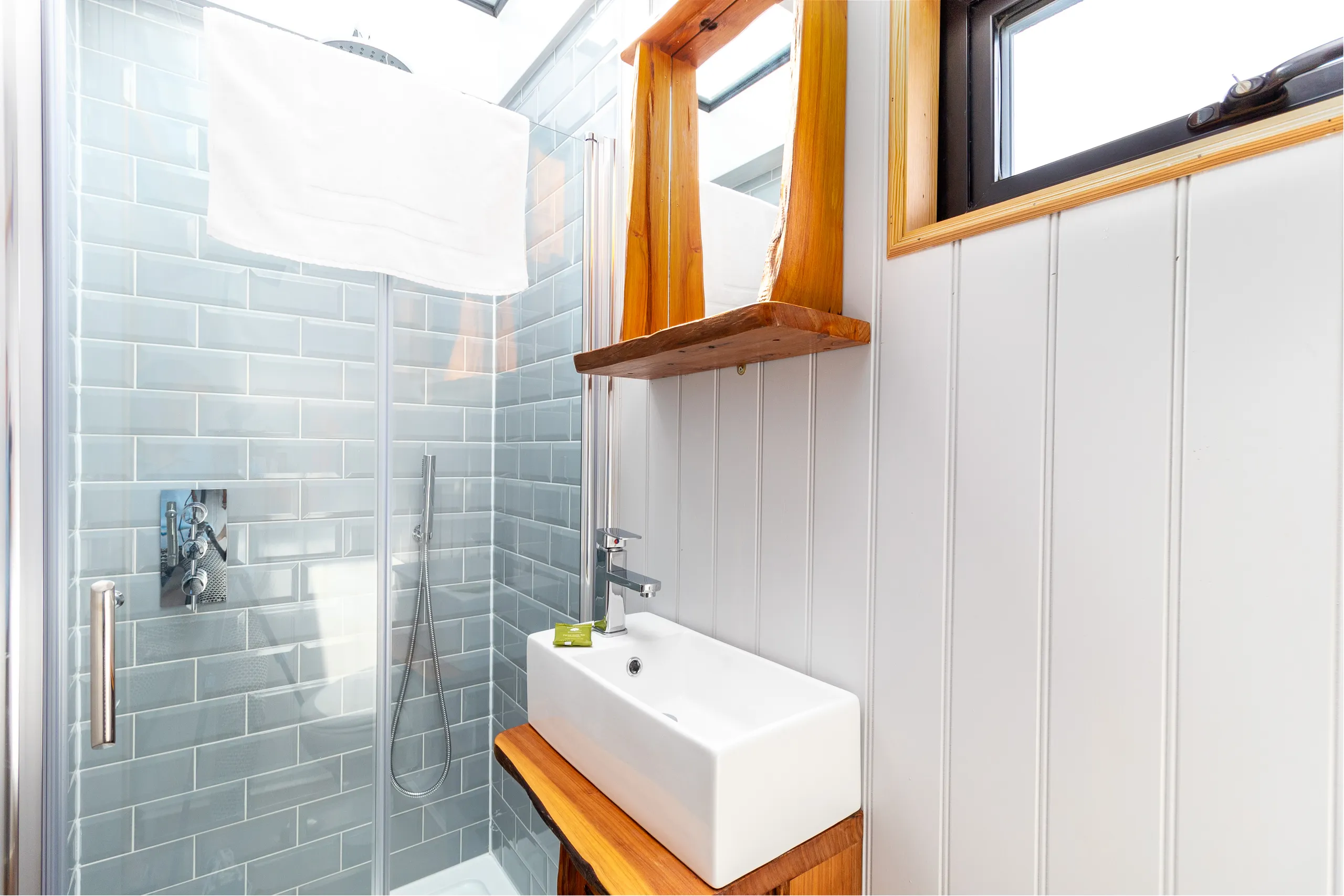 Bright modern bathroom with glass shower, grey subway tiles, and white basin on a wooden vanity