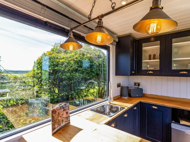 Modern kitchen with navy cabinets, wooden worktops and pendant lights beside a large window overlooking greenery