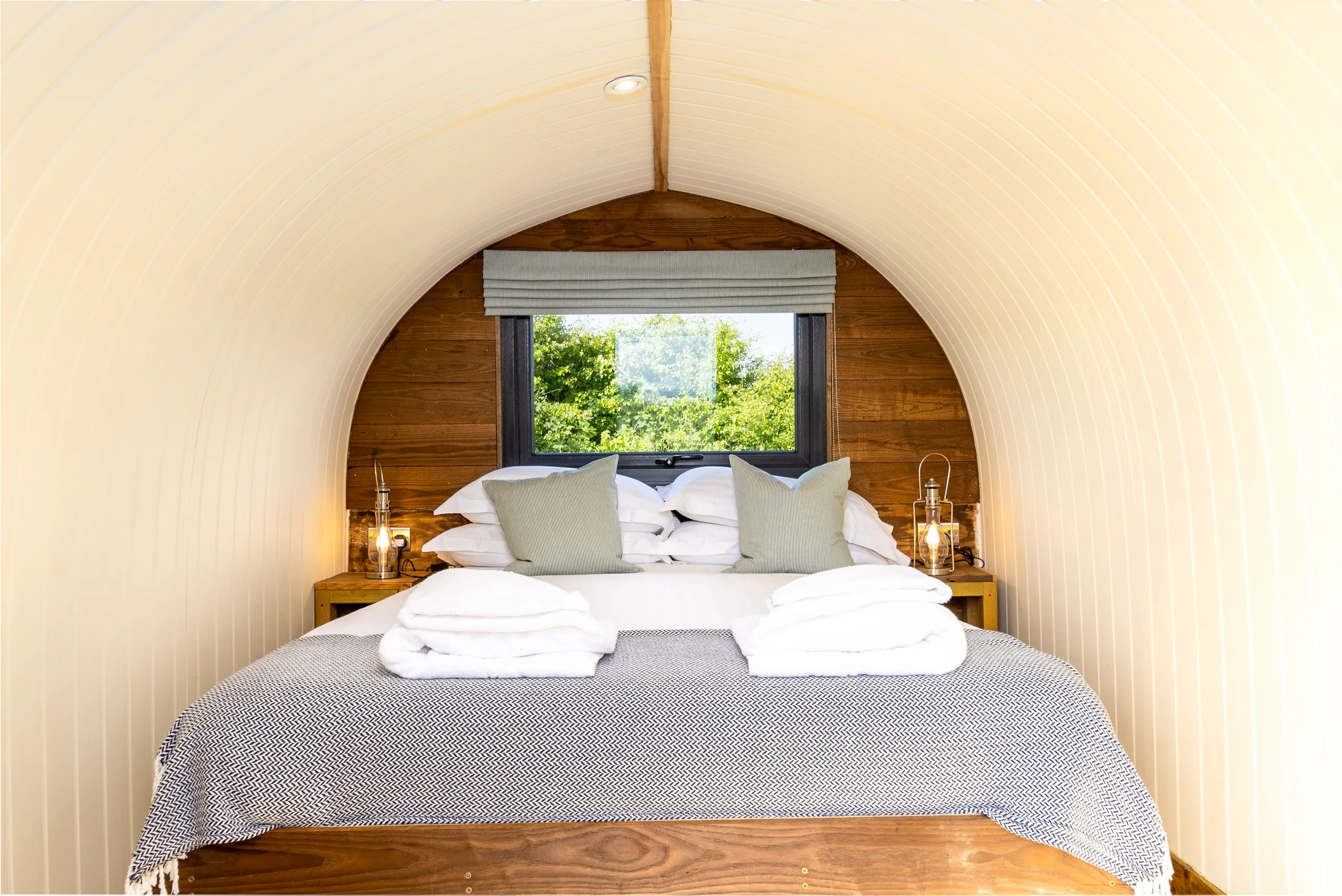 Cosy double bed inside an arched glamping pod with window view and lantern bedside lights