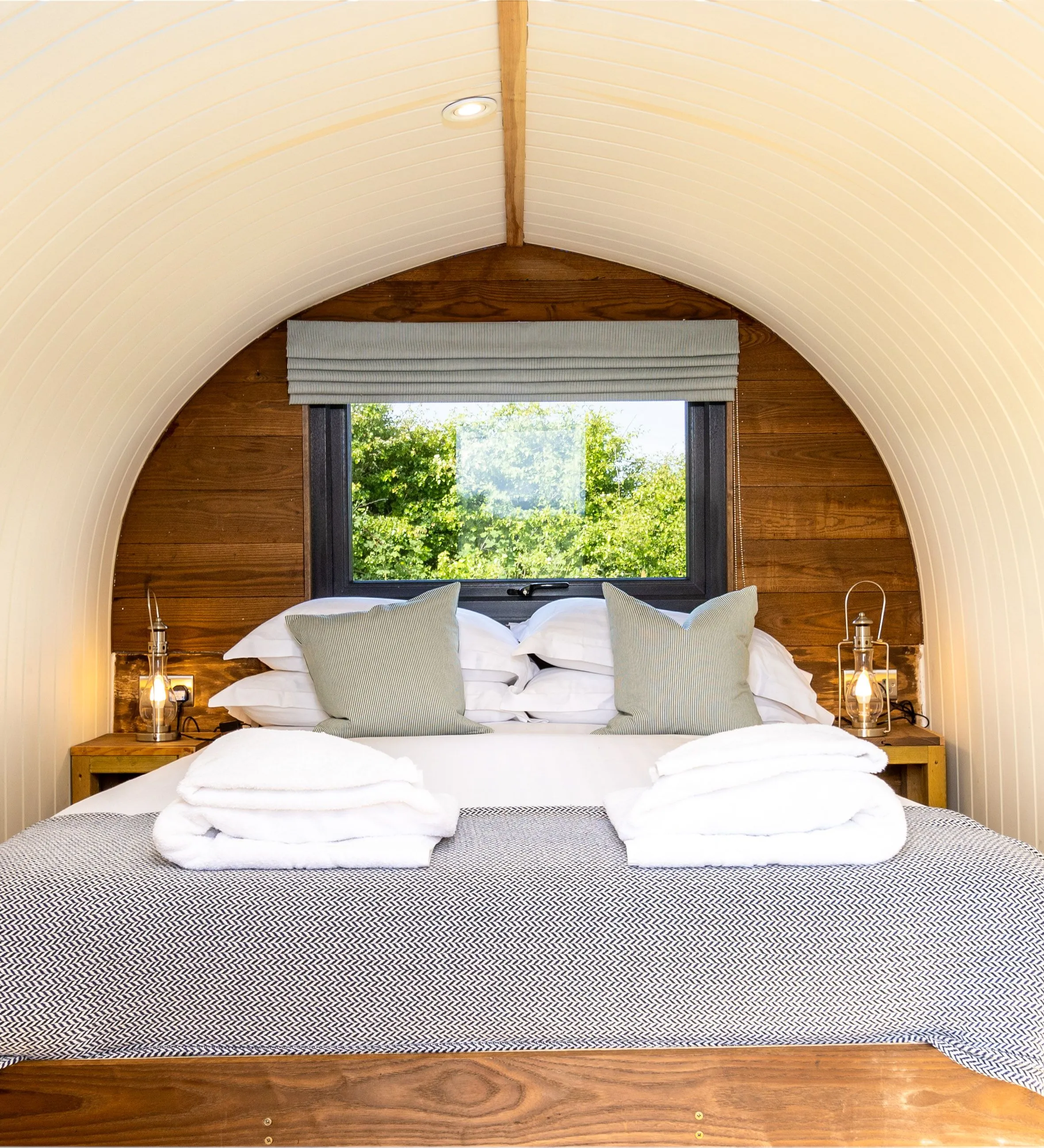Cosy double bed inside an arched glamping pod with window view and lantern bedside lights