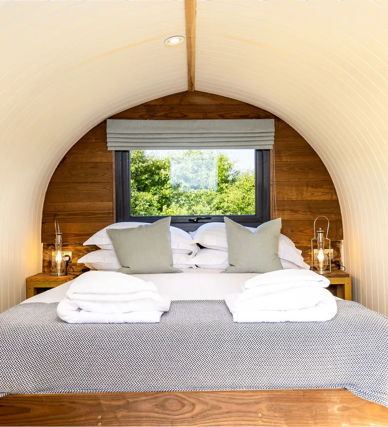 Cosy double bed inside an arched glamping pod with window view and lantern bedside lights