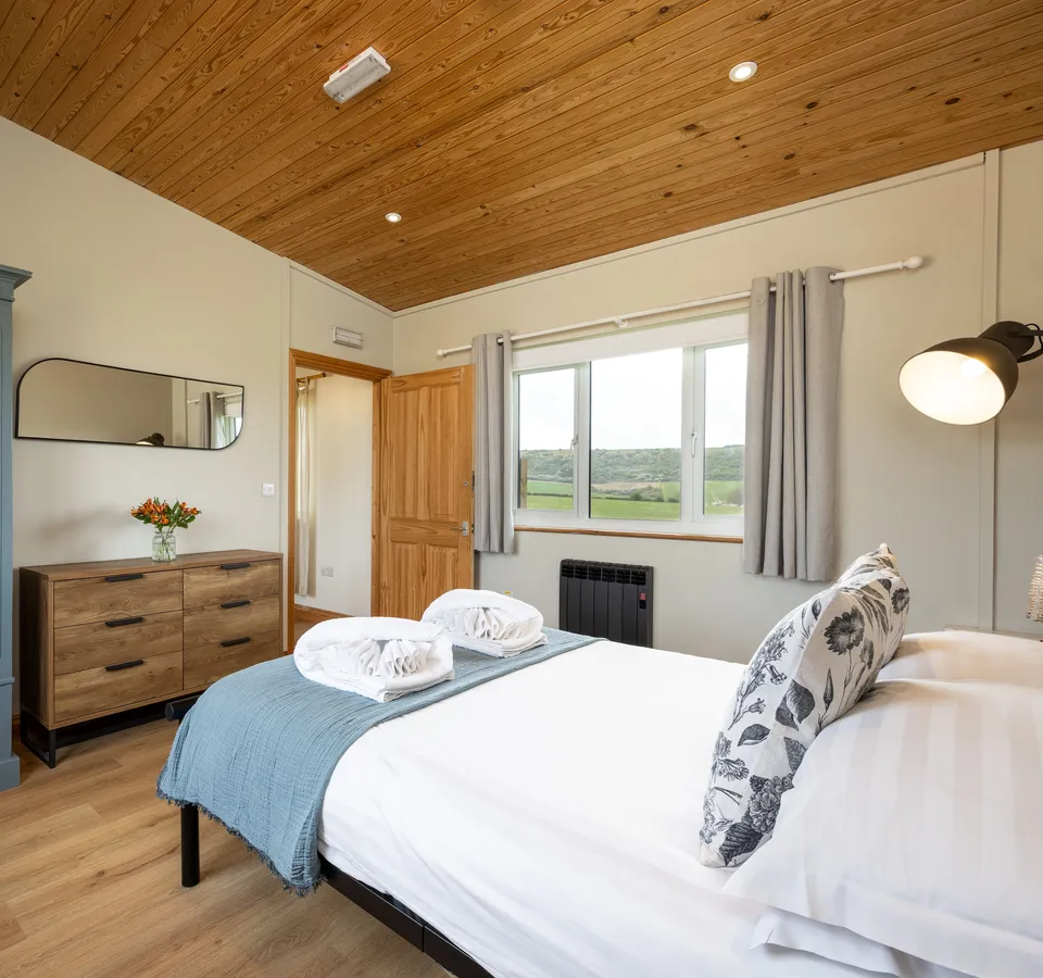 Cosy bedroom with double bed, blue throw, grey wardrobe and countryside view through the window