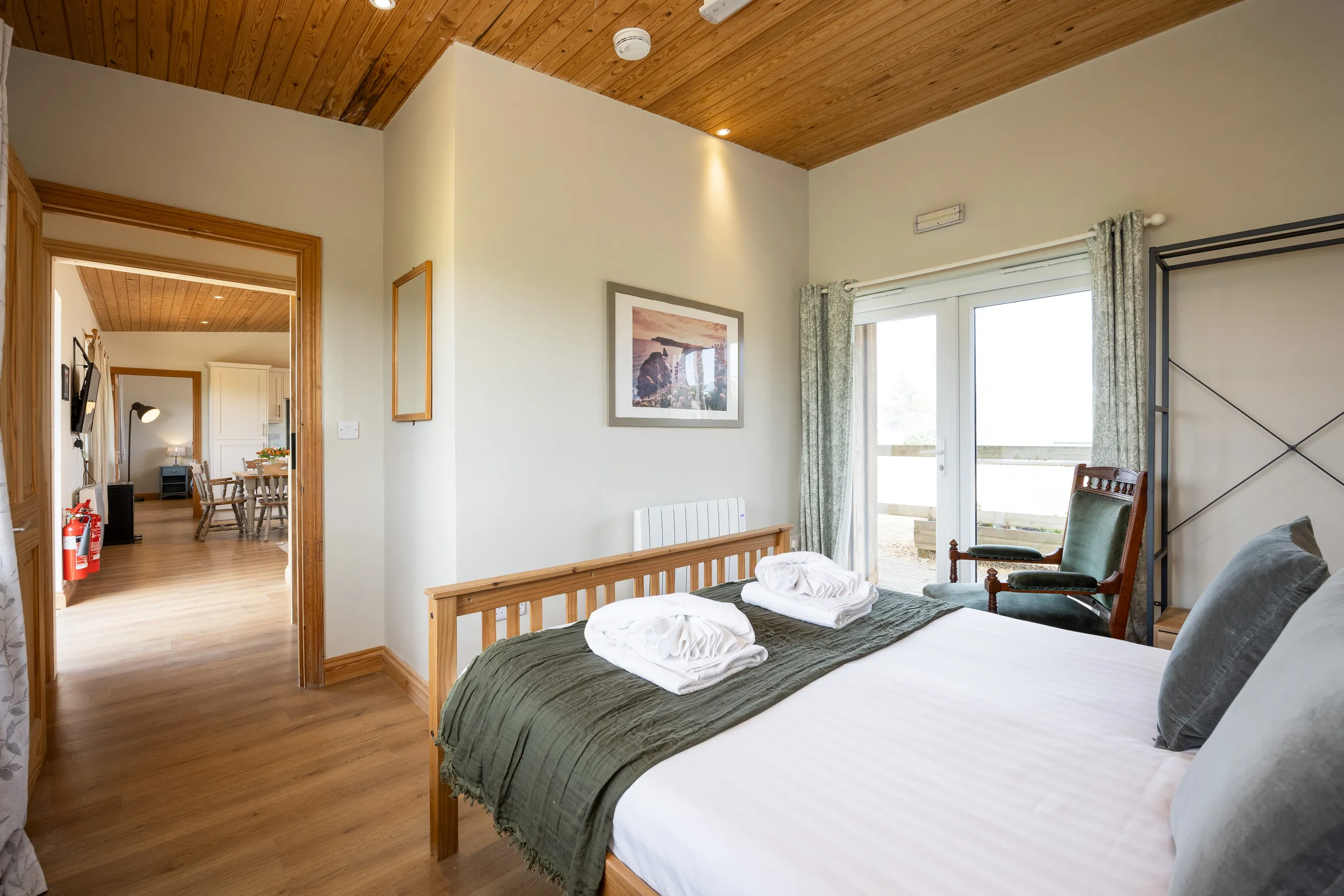 Cosy bedroom with wooden ceiling, double bed with folded towels, and French doors to an outdoor area