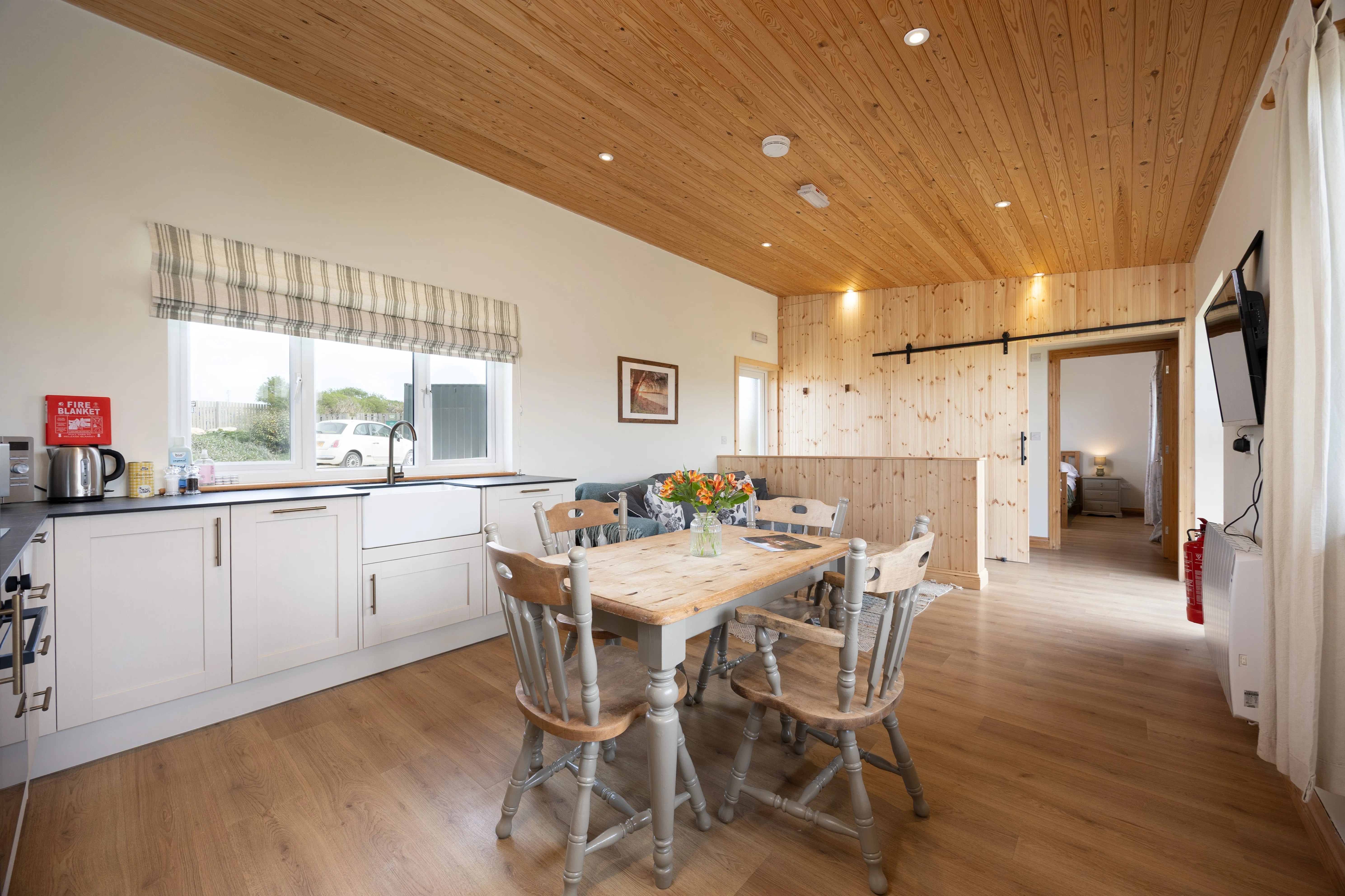 Open-plan lodge kitchen and dining area with wooden ceiling, farmhouse table and large window