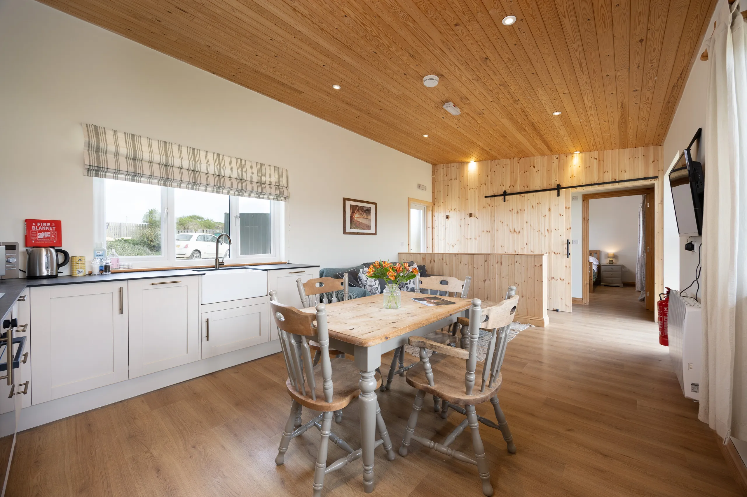 Open-plan lodge kitchen and dining area with wooden ceiling, farmhouse table and large window