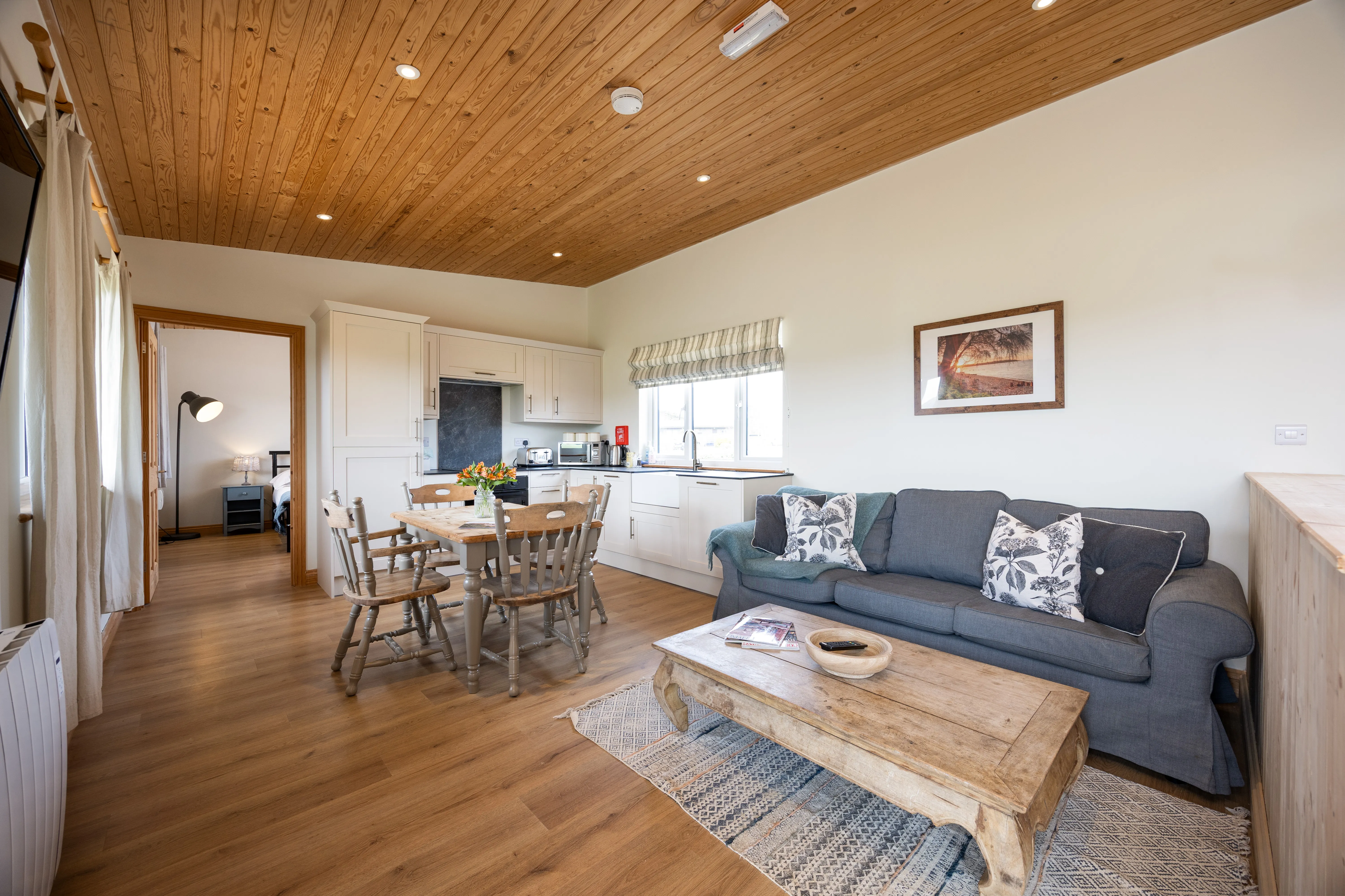 Open-plan lodge living room and kitchen with wooden ceiling, dining table and grey sofa