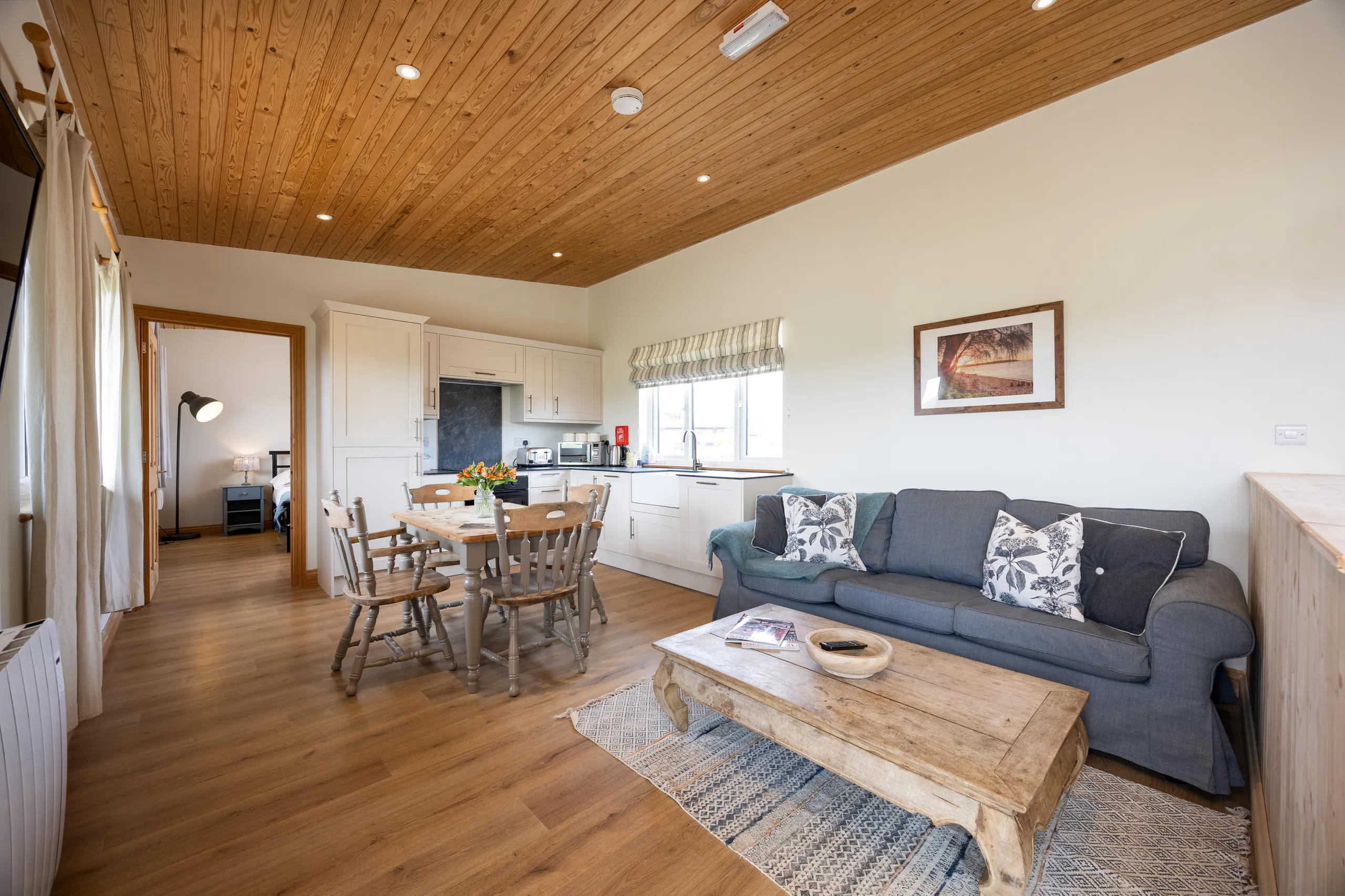 Open-plan lodge living room and kitchen with wooden ceiling, dining table and grey sofa