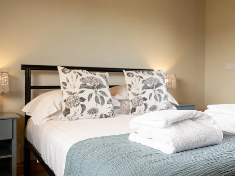Cosy bedroom with double bed, floral cushions and folded white towels on a blue throw