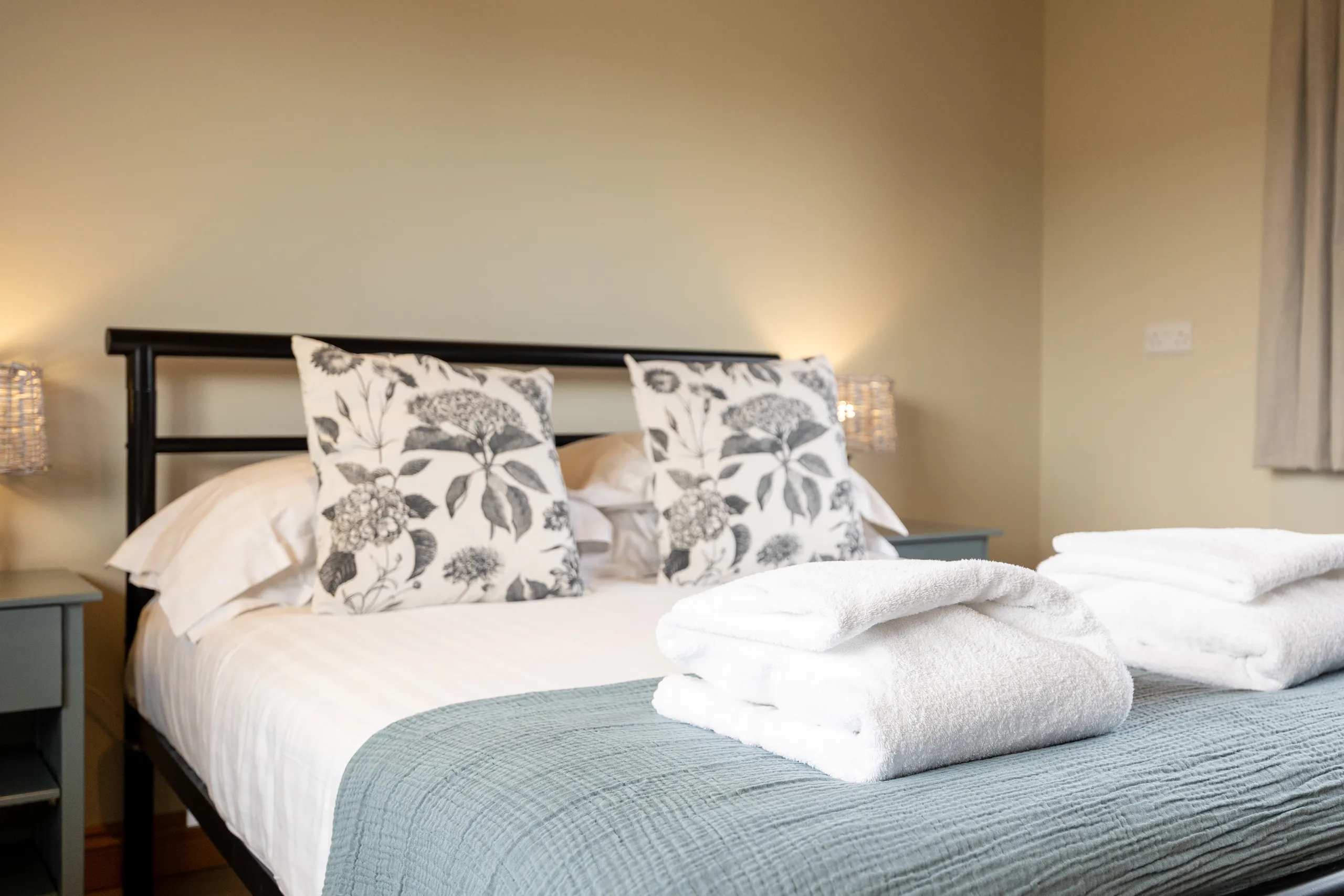 Cosy bedroom with double bed, floral cushions and folded white towels on a blue throw