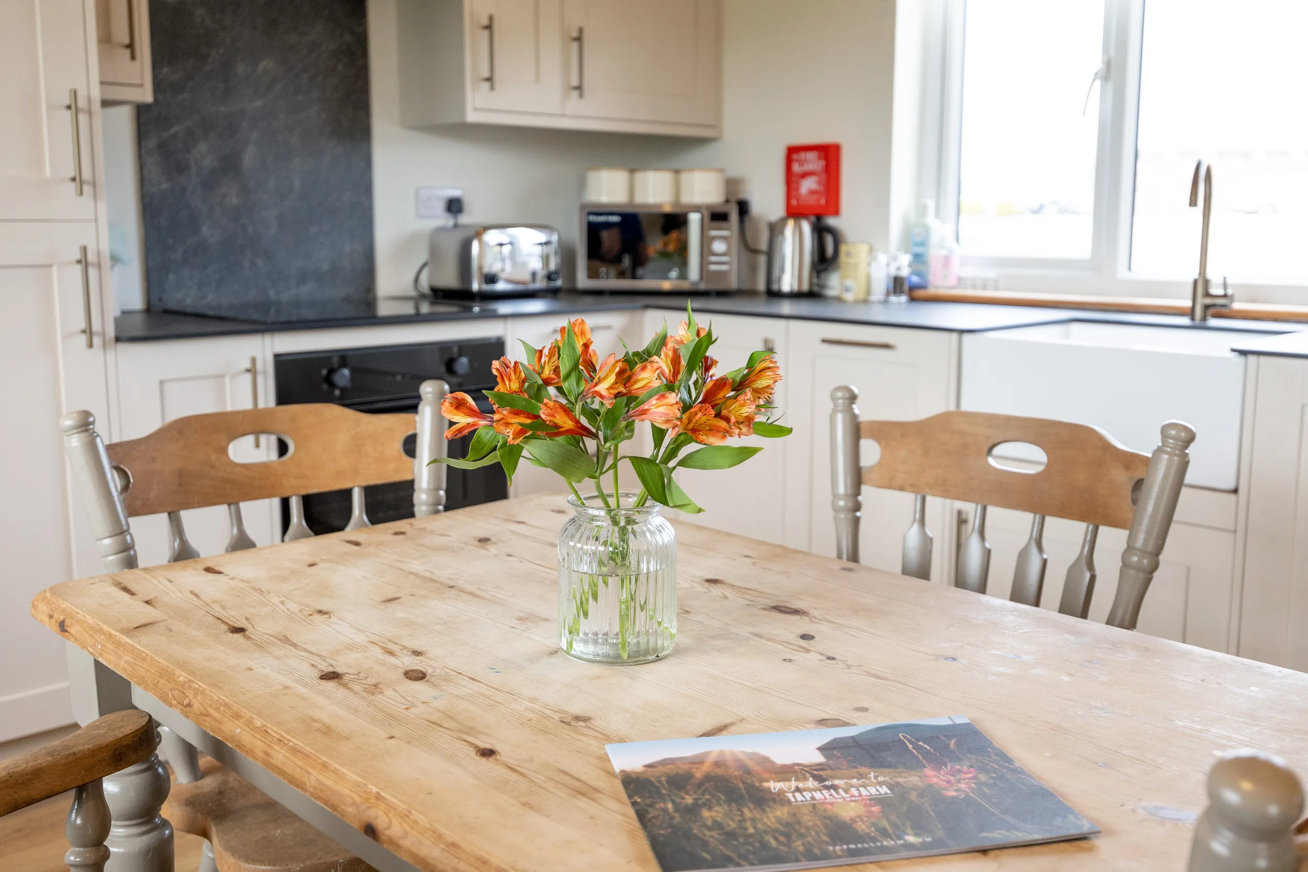 Wooden dining table with a vase of orange flowers in a bright, modern kitchen